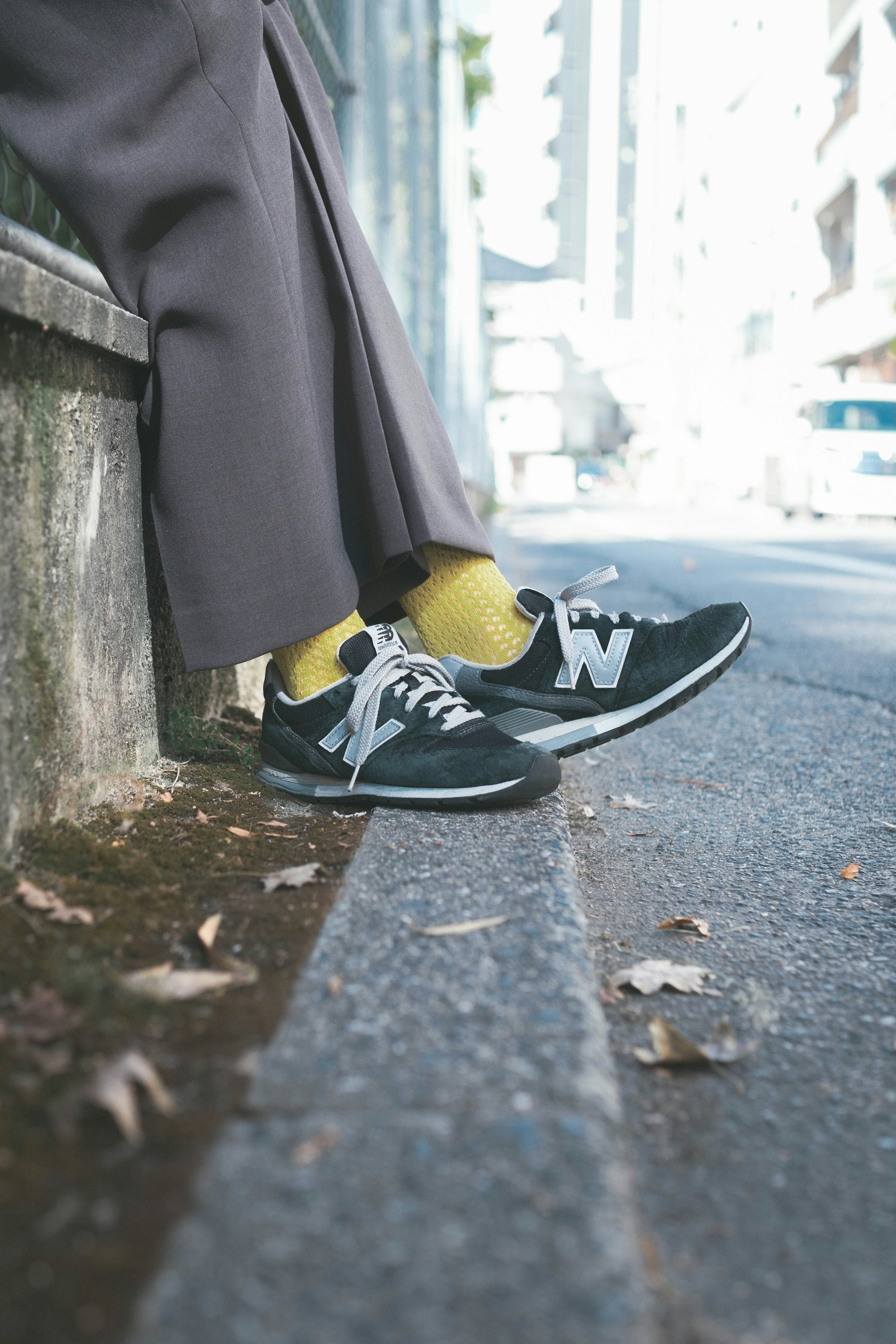 Feet in black New Balance sneakers and yellow socks resting on the sidewalk