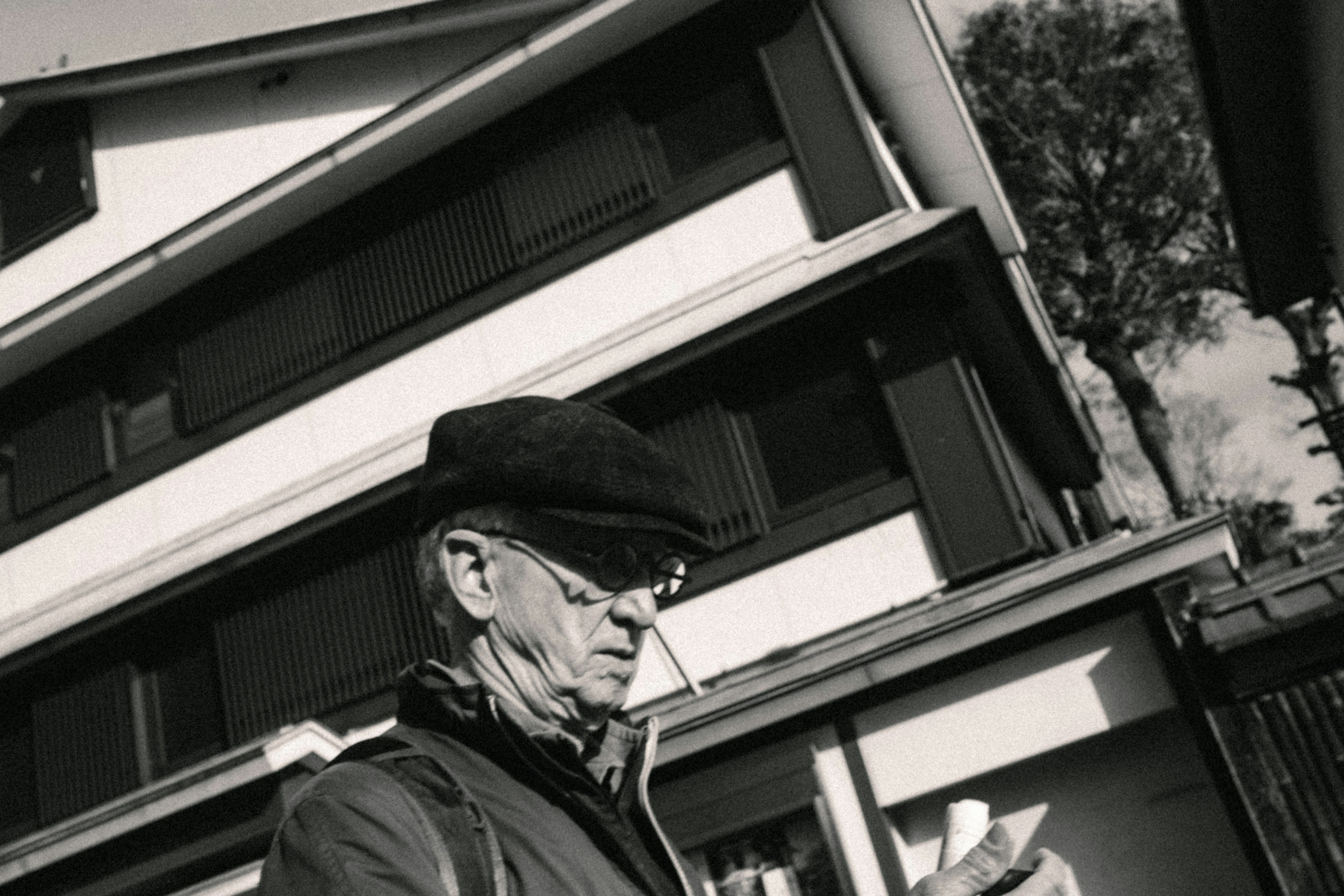 Hombre anciano con sombrero negro mirando un teléfono frente a un edificio