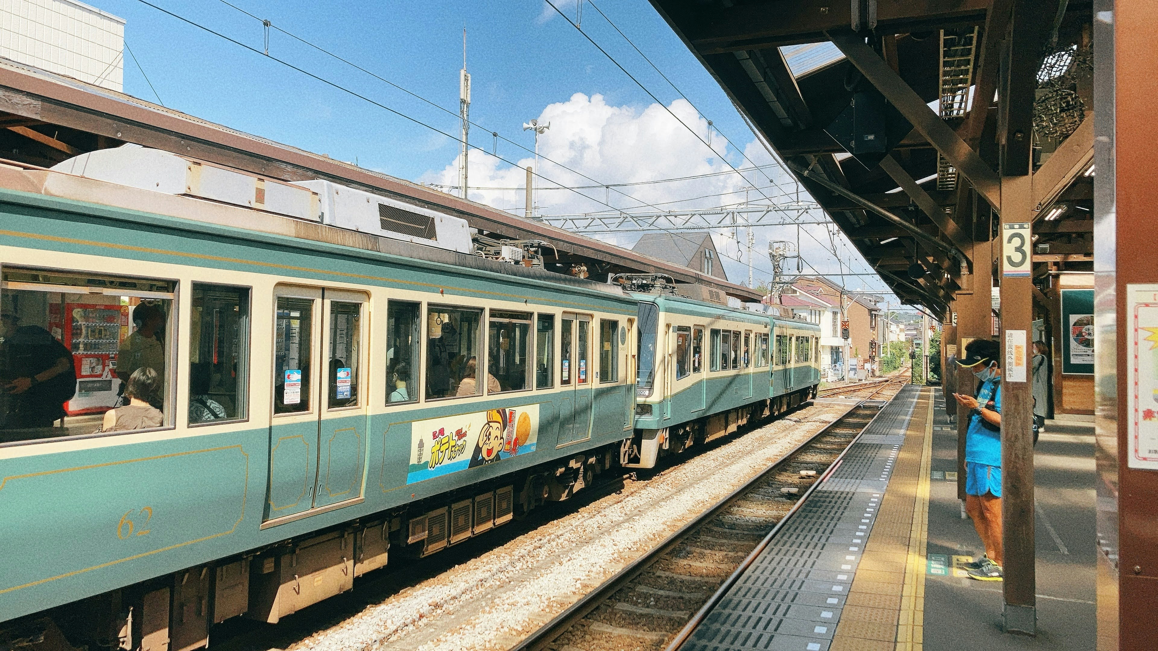 Un treno verde in arrivo a una stazione con cielo soleggiato