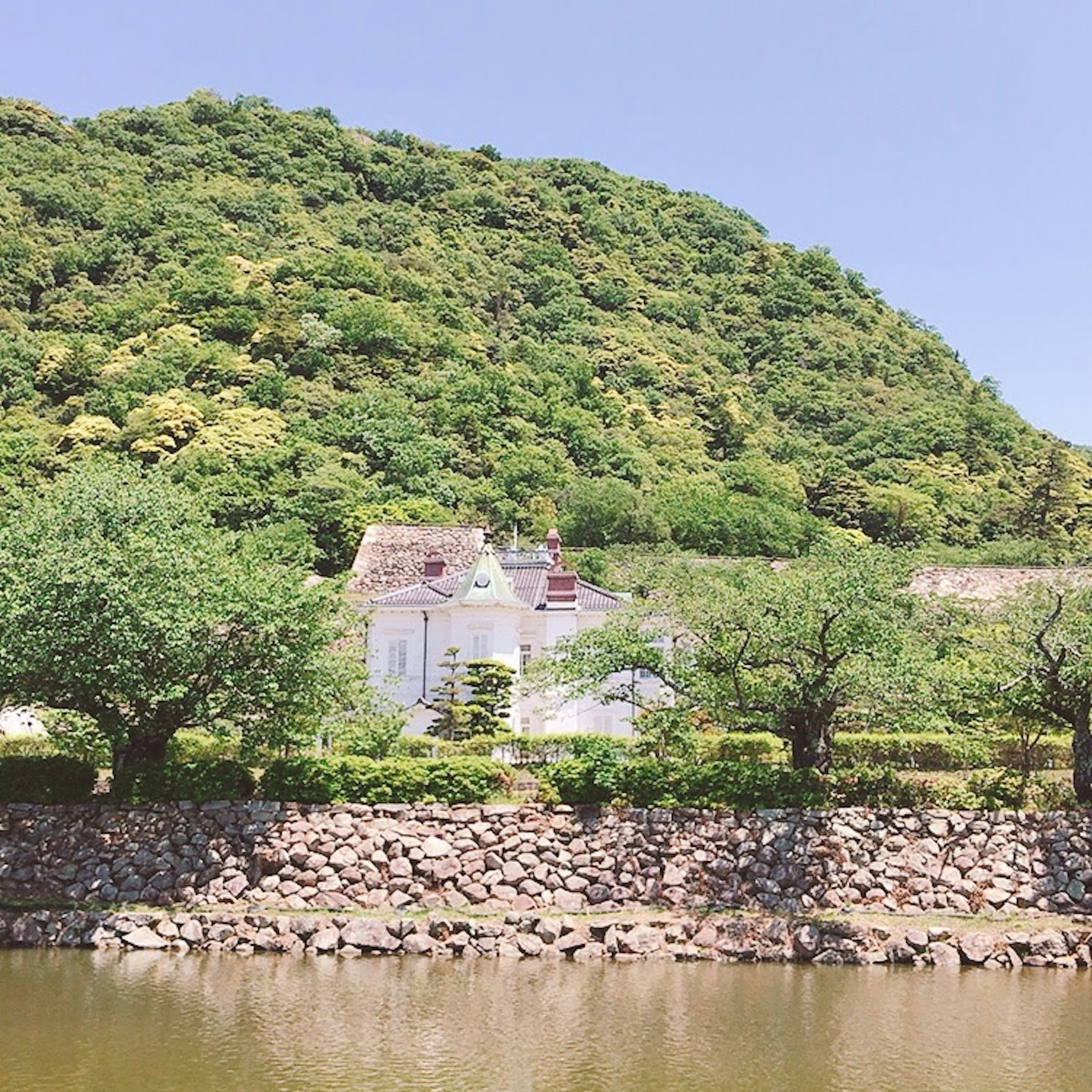 A white house with a green mountain backdrop and a stone embankment