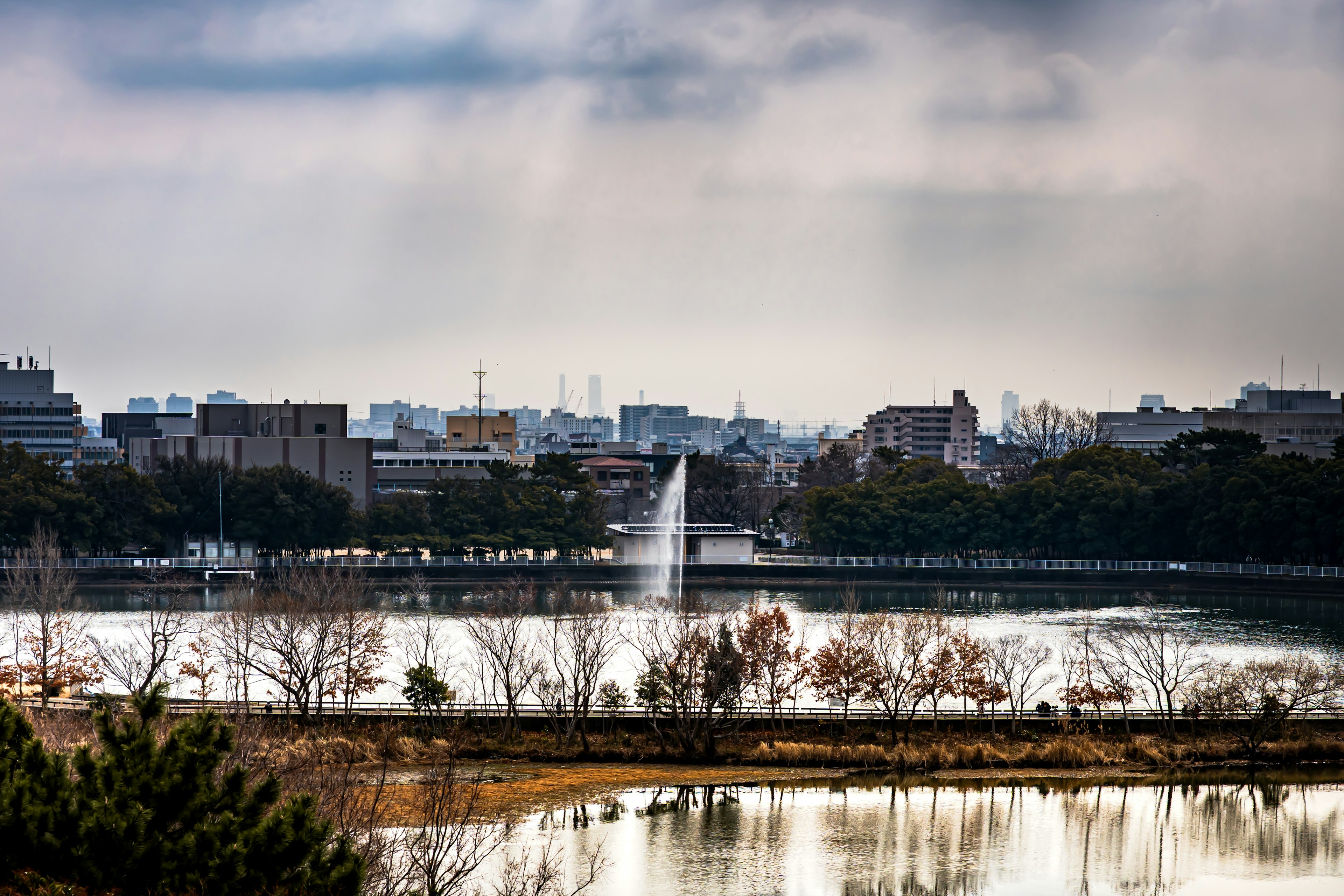 公園湖泊的風景，噴泉周圍是城市建築和陰天