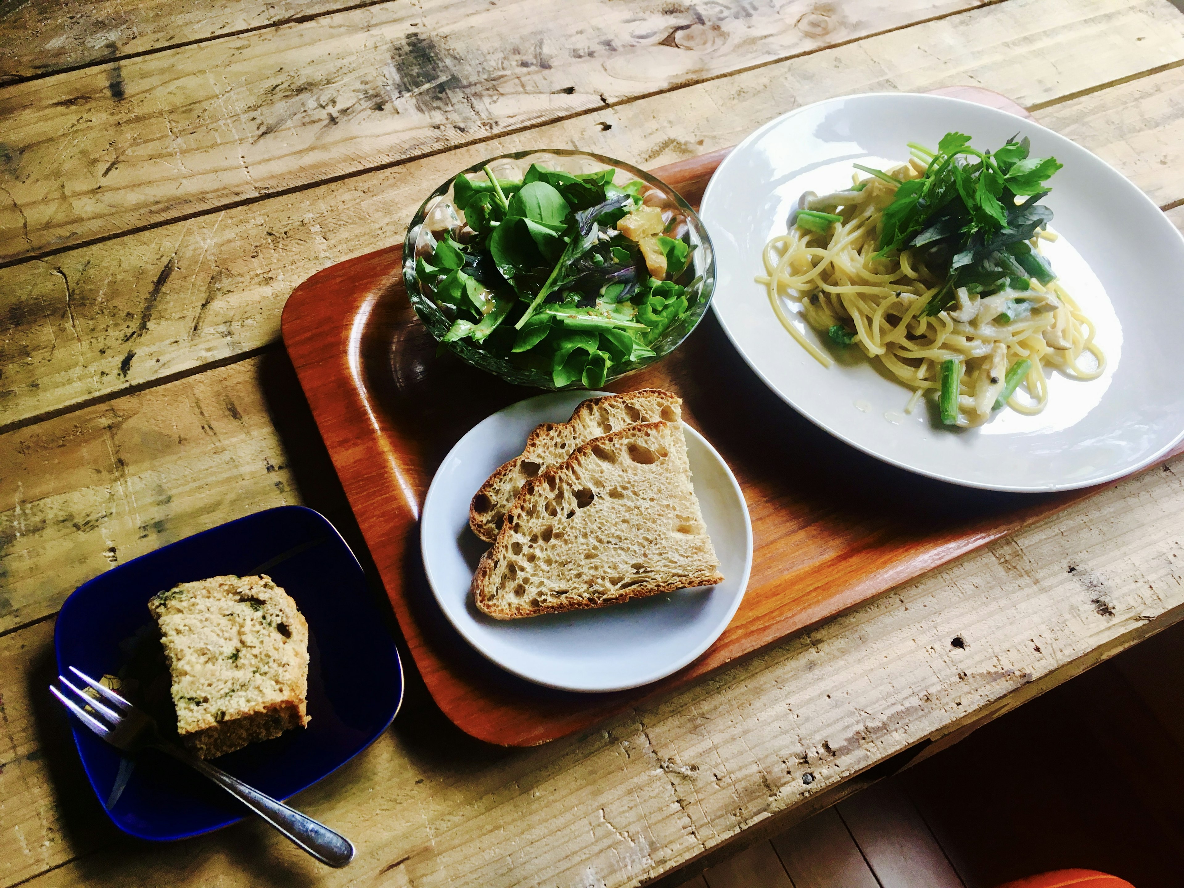 Tray featuring salad, pasta, and bread on a wooden table