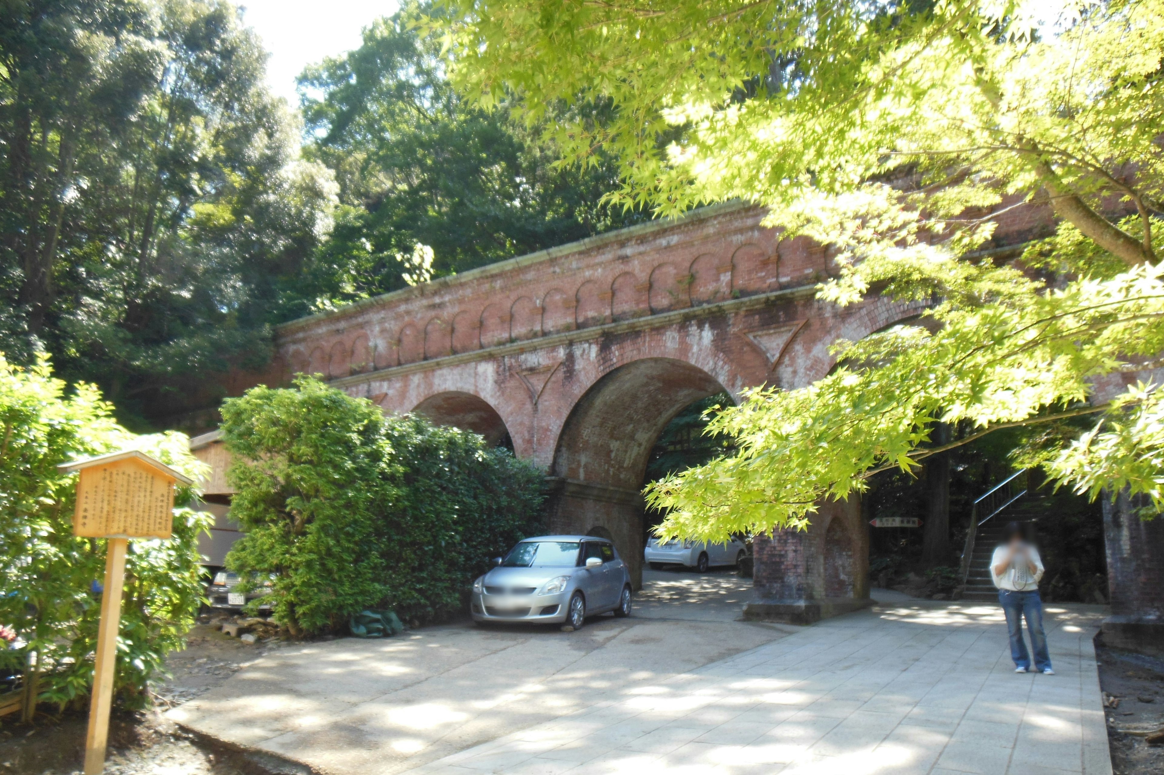 Red brick arch bridge surrounded by greenery with parked cars