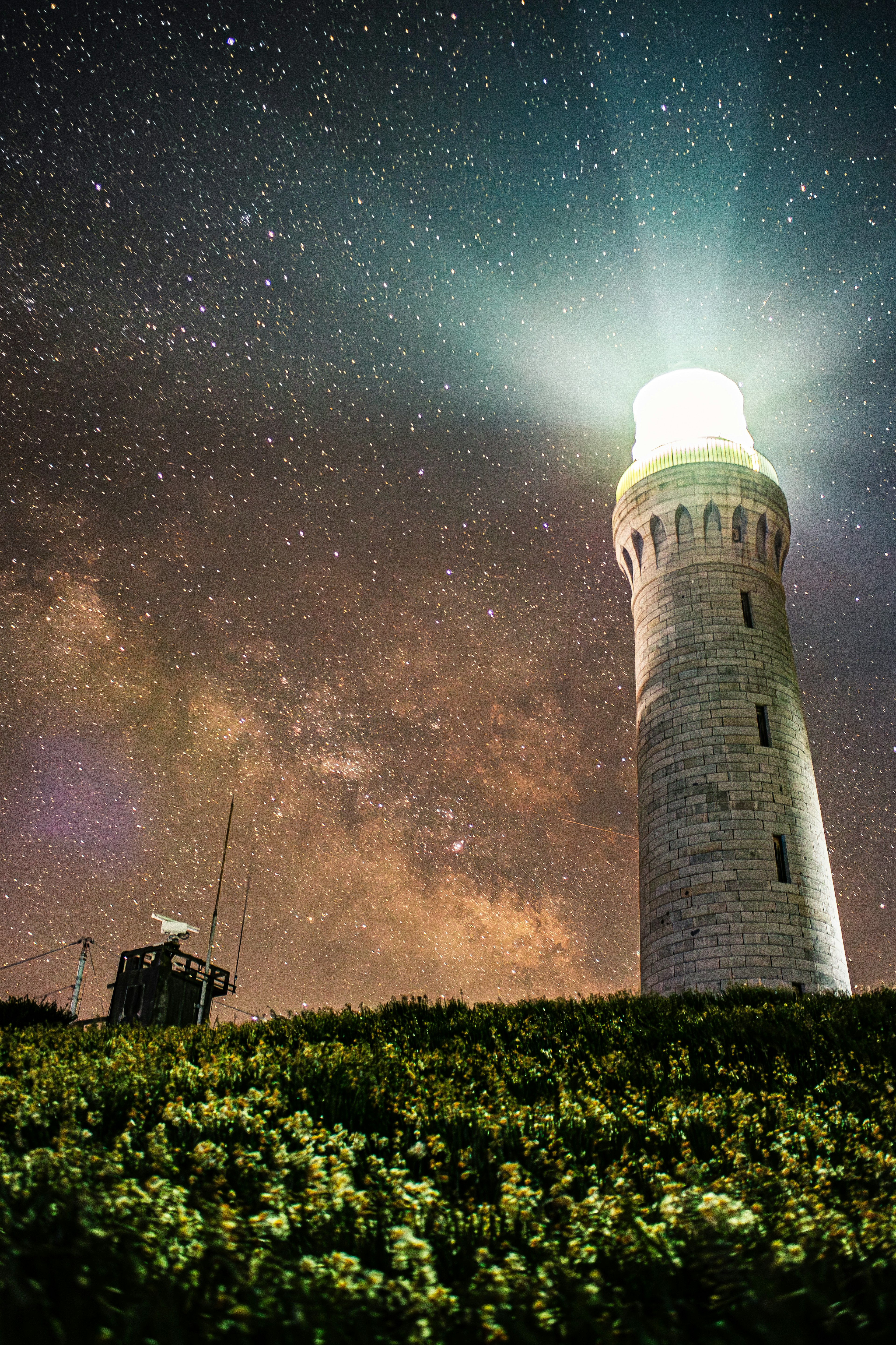 星空の下に立つ灯台とその光が輝いている