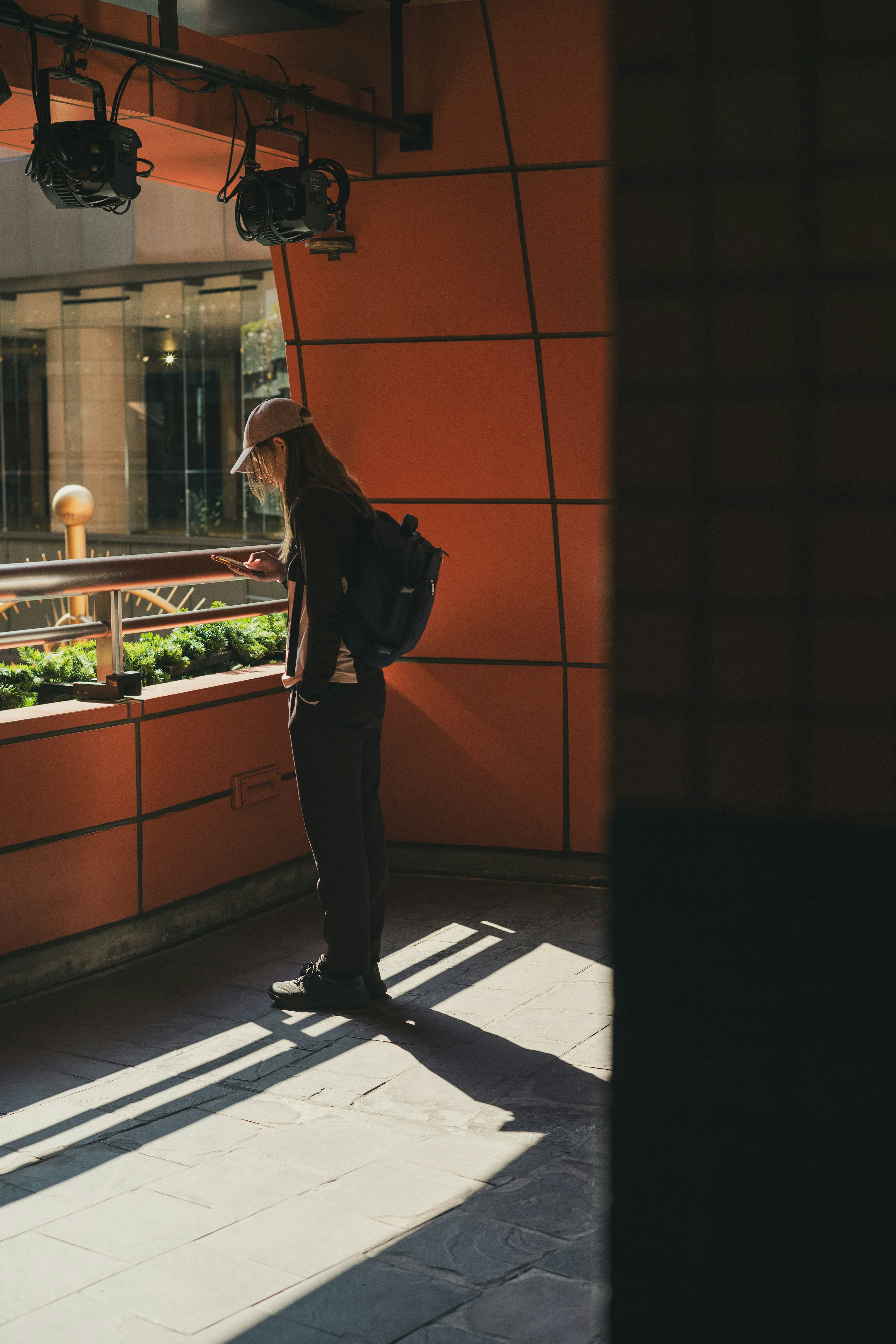 Eine Figur steht an einer orangefarbenen Wand mit Sonnenlicht, das durch ein Fenster strömt