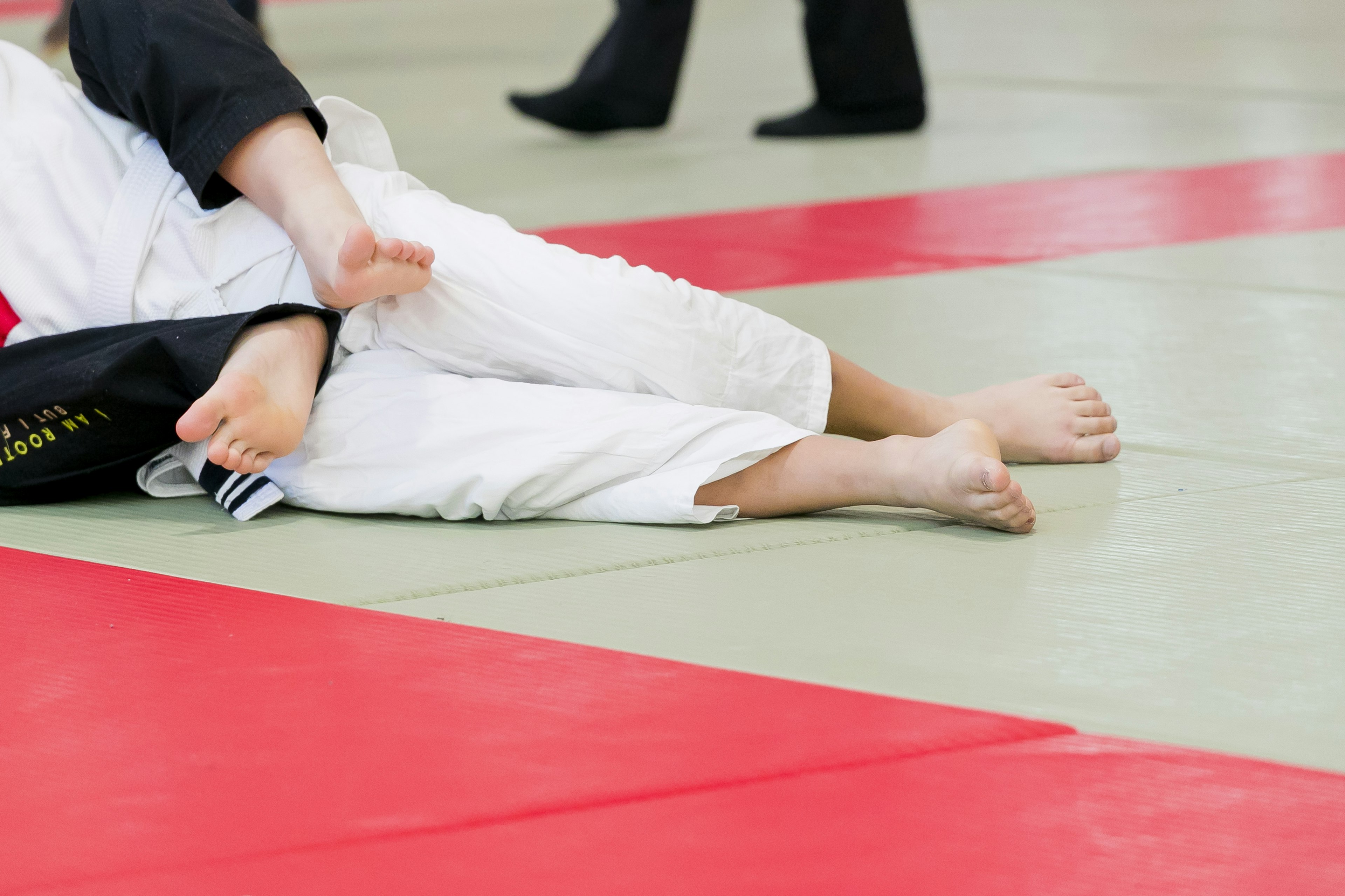 Primo piano dei piedi di un judoka sul tatami indossando un gi bianco con tatami rossi