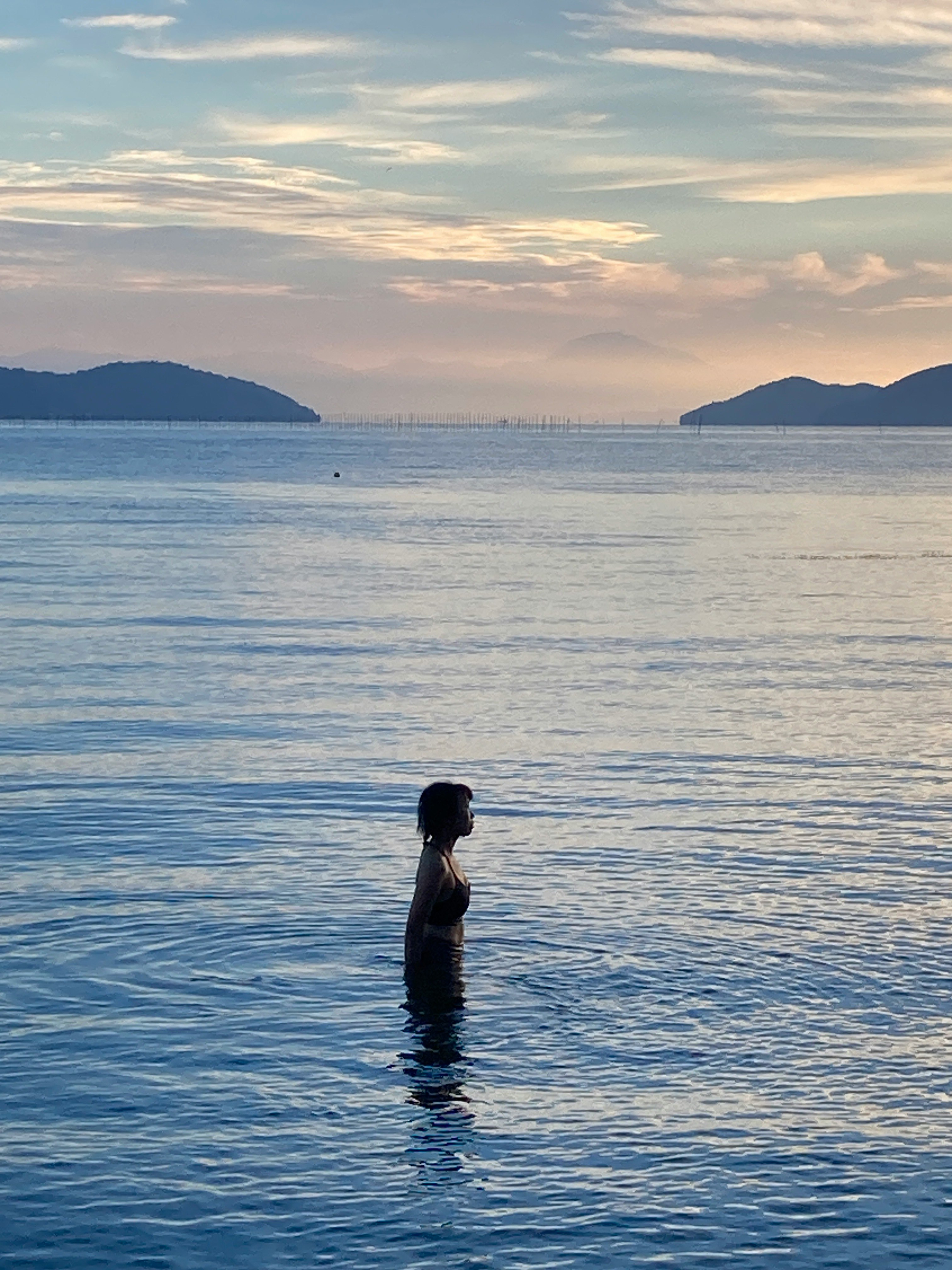 夕暮れ時の海に立つ人物のシルエットと穏やかな水面