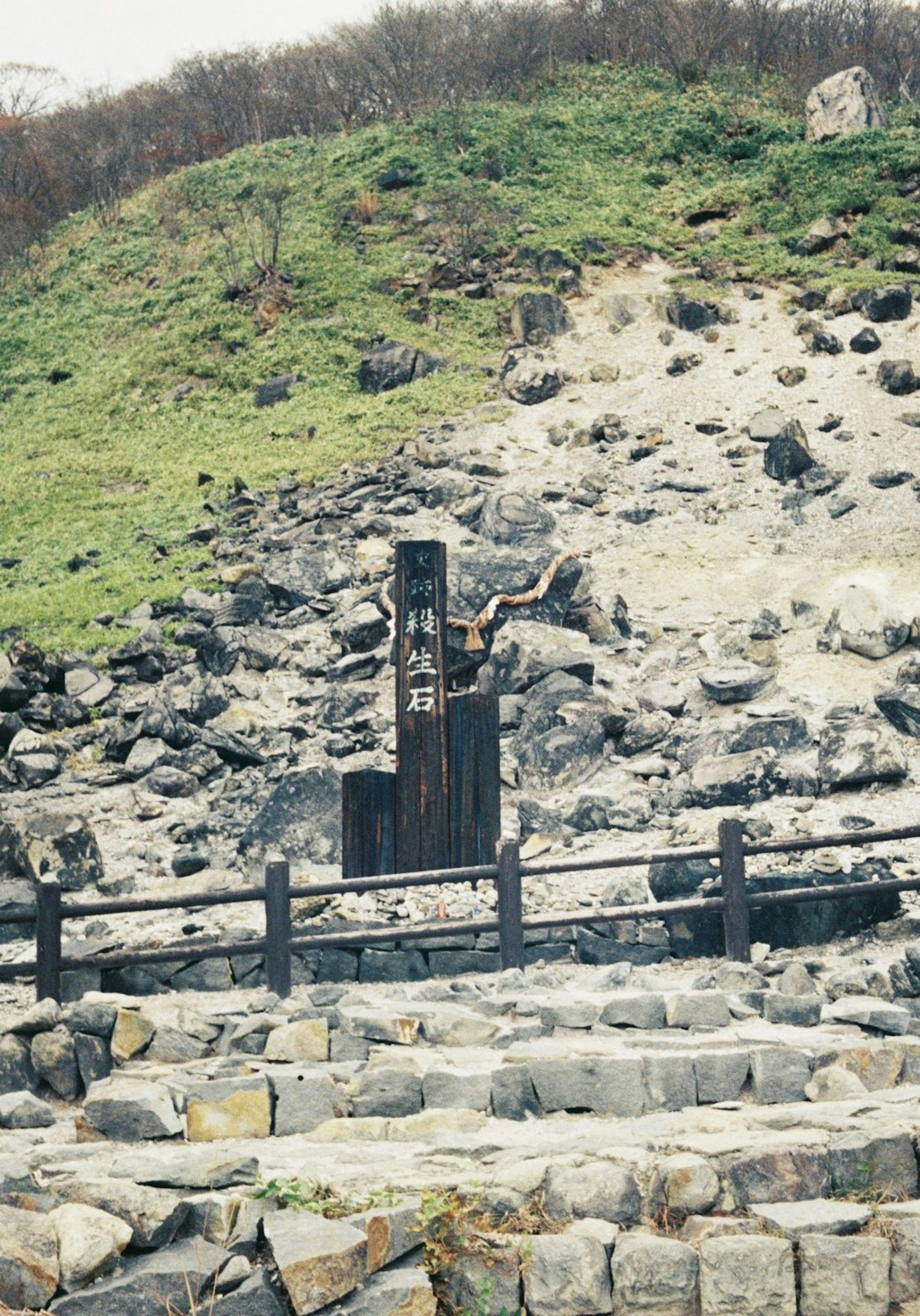 Pemandangan dengan struktur kayu di antara batuan dan bukit hijau