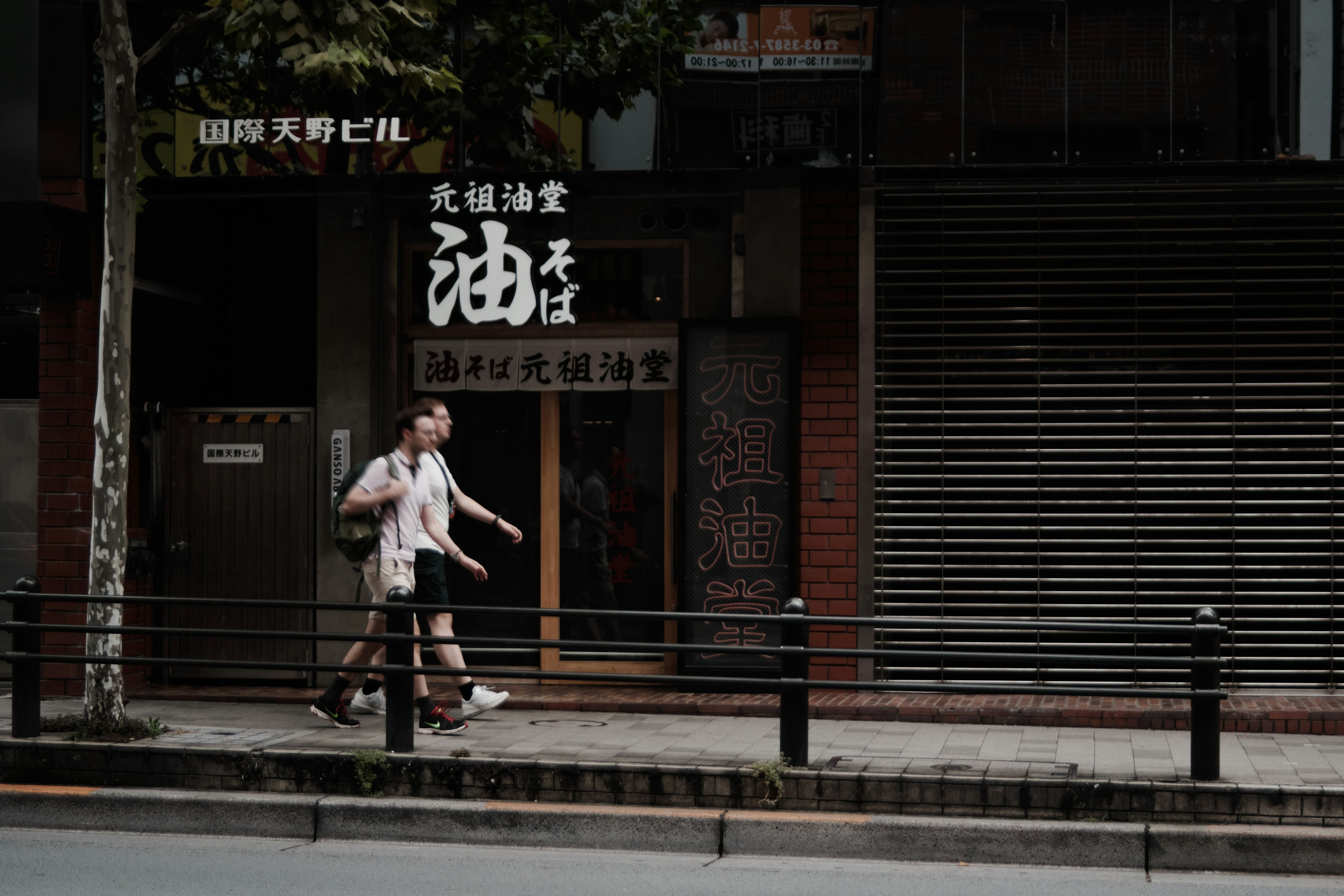 A person walking on the street in front of a closed shop with Japanese signage