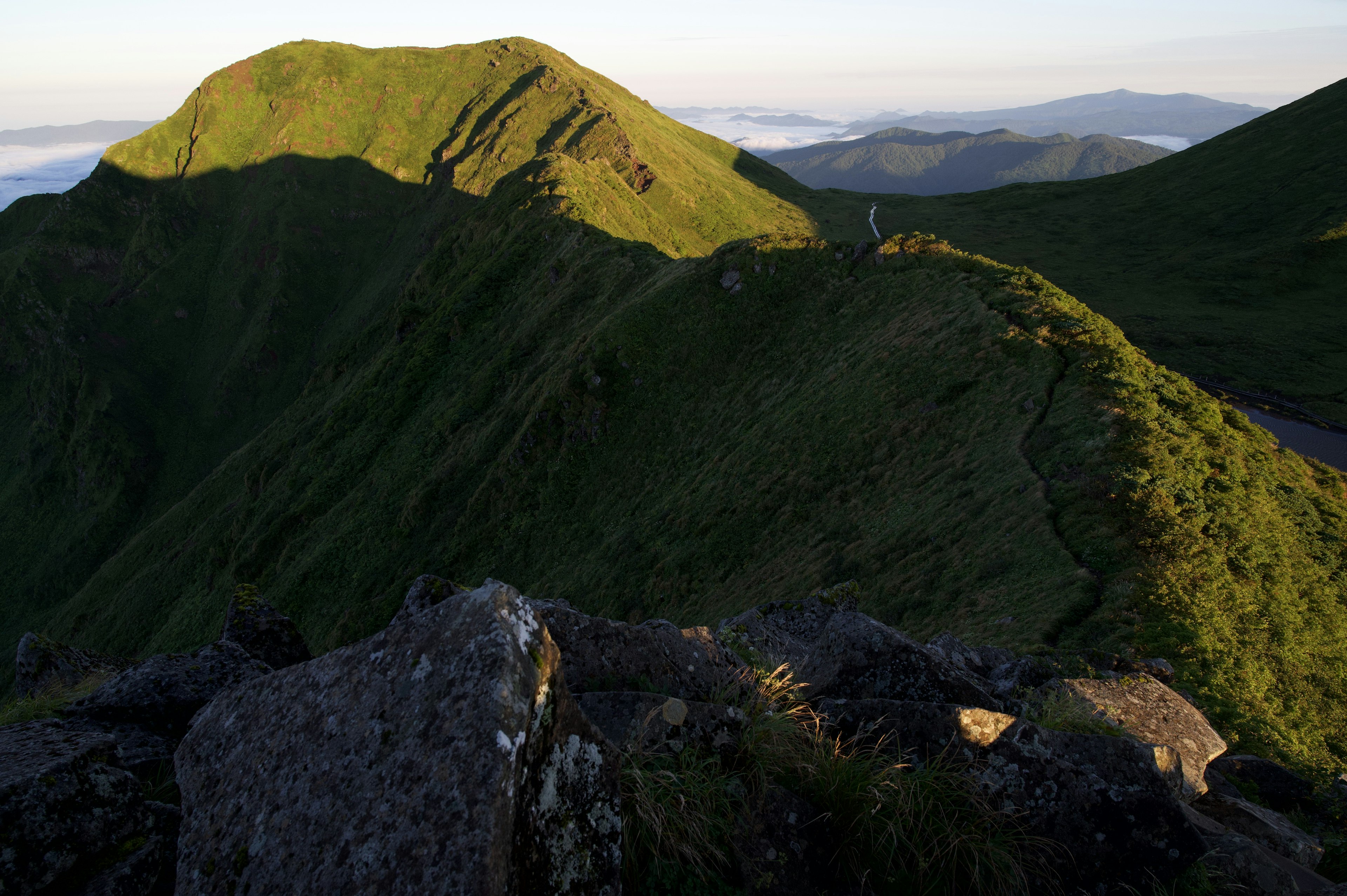 Vue panoramique de montagnes vertes avec un premier plan rocheux et un jeu de lumière et d'ombre