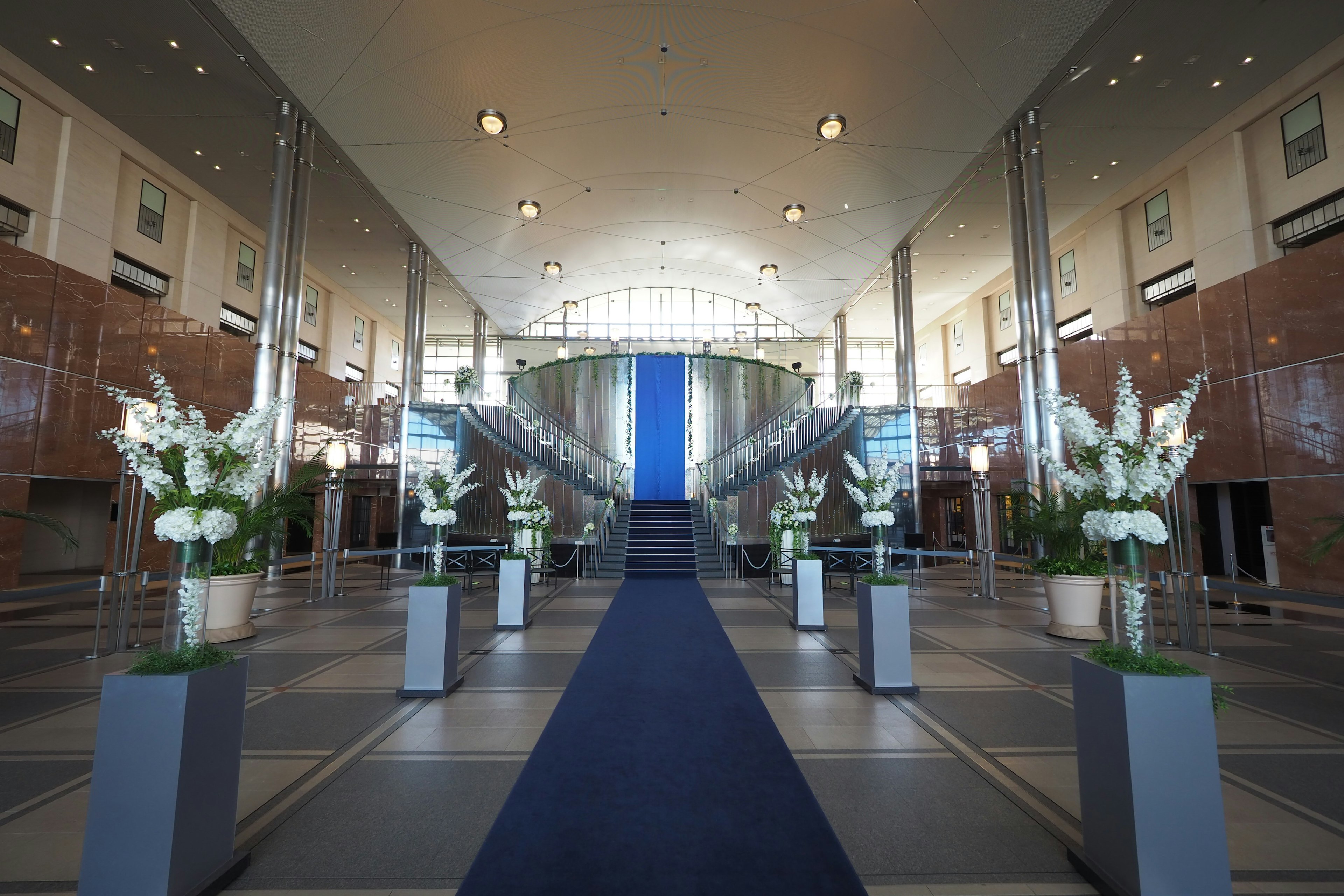 Intérieur spacieux du hall avec tapis bleu, arrangements floraux blancs, éclairage lumineux