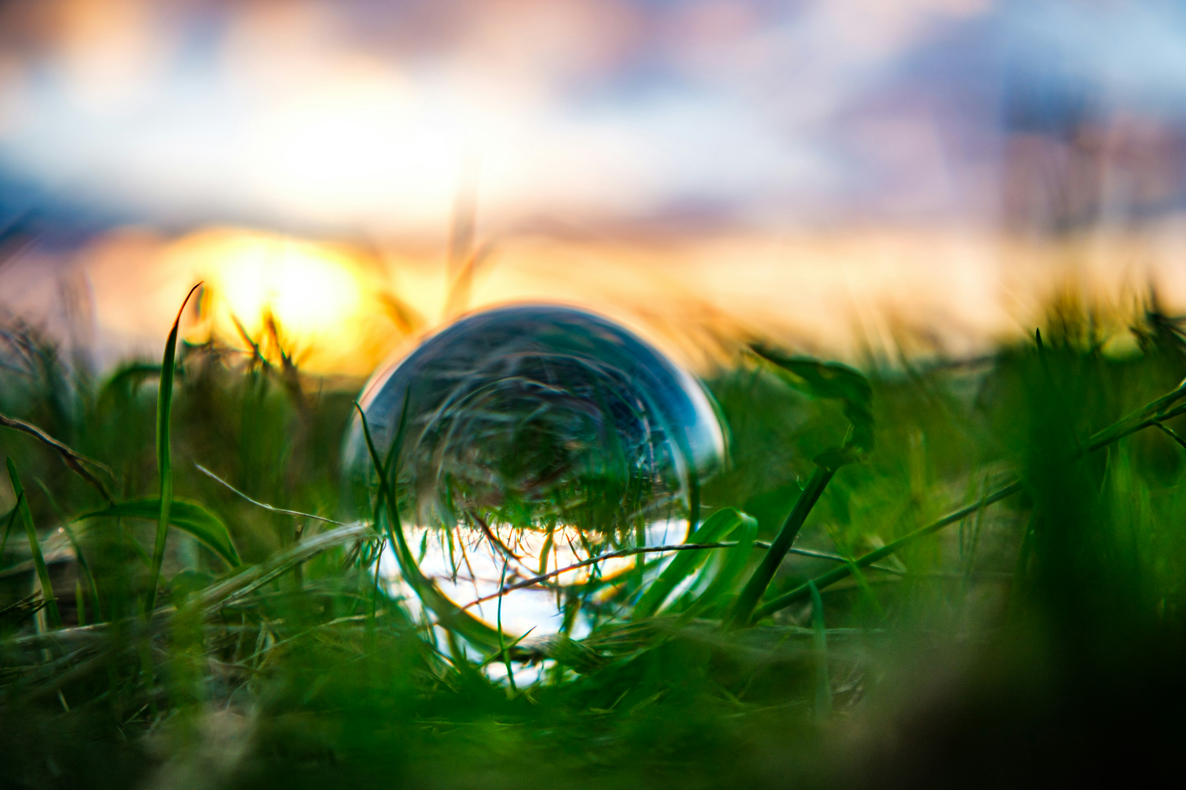 A clear glass sphere resting on grass with a beautiful sunset in the background