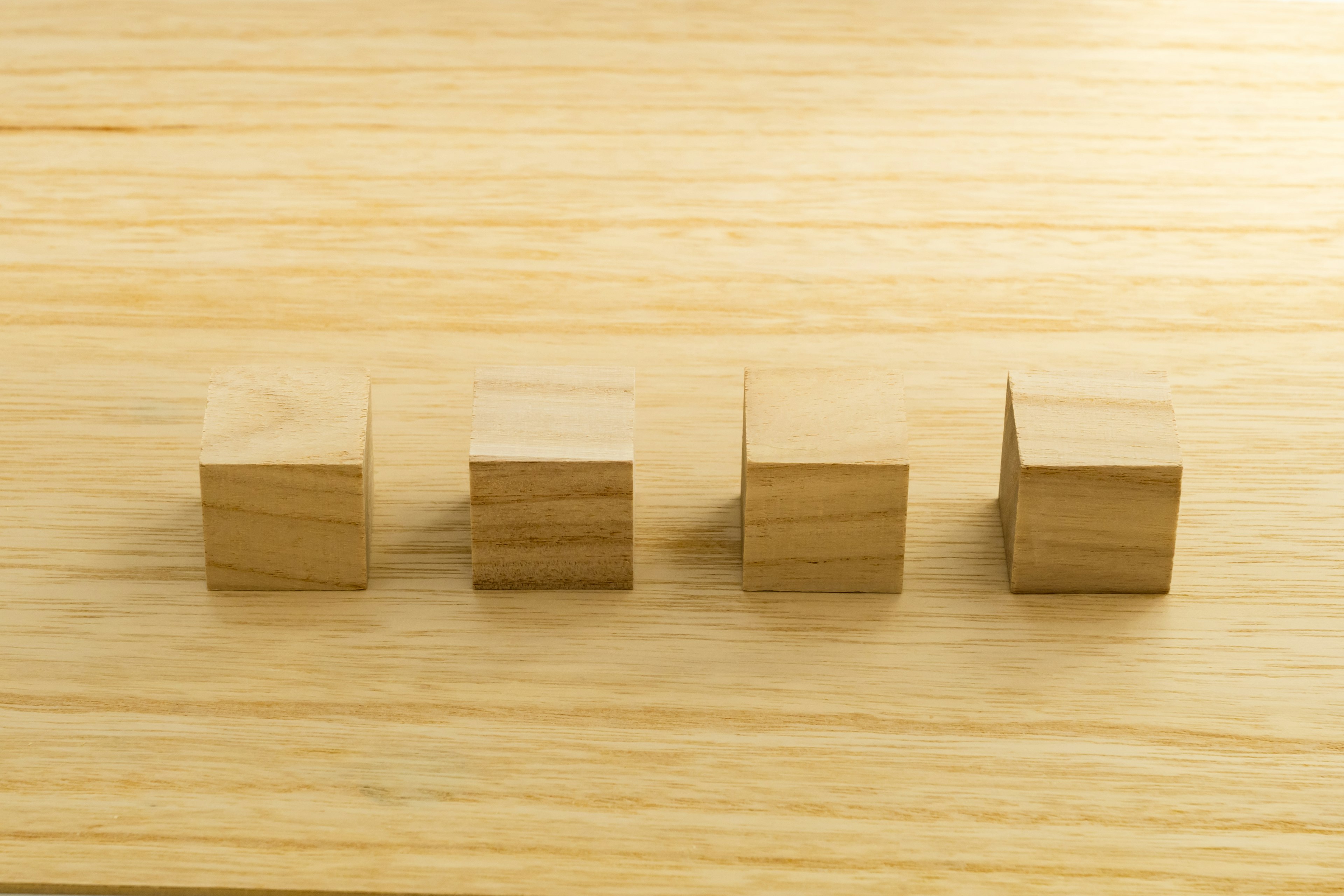 Four wooden cubes arranged in a row on a light wooden surface