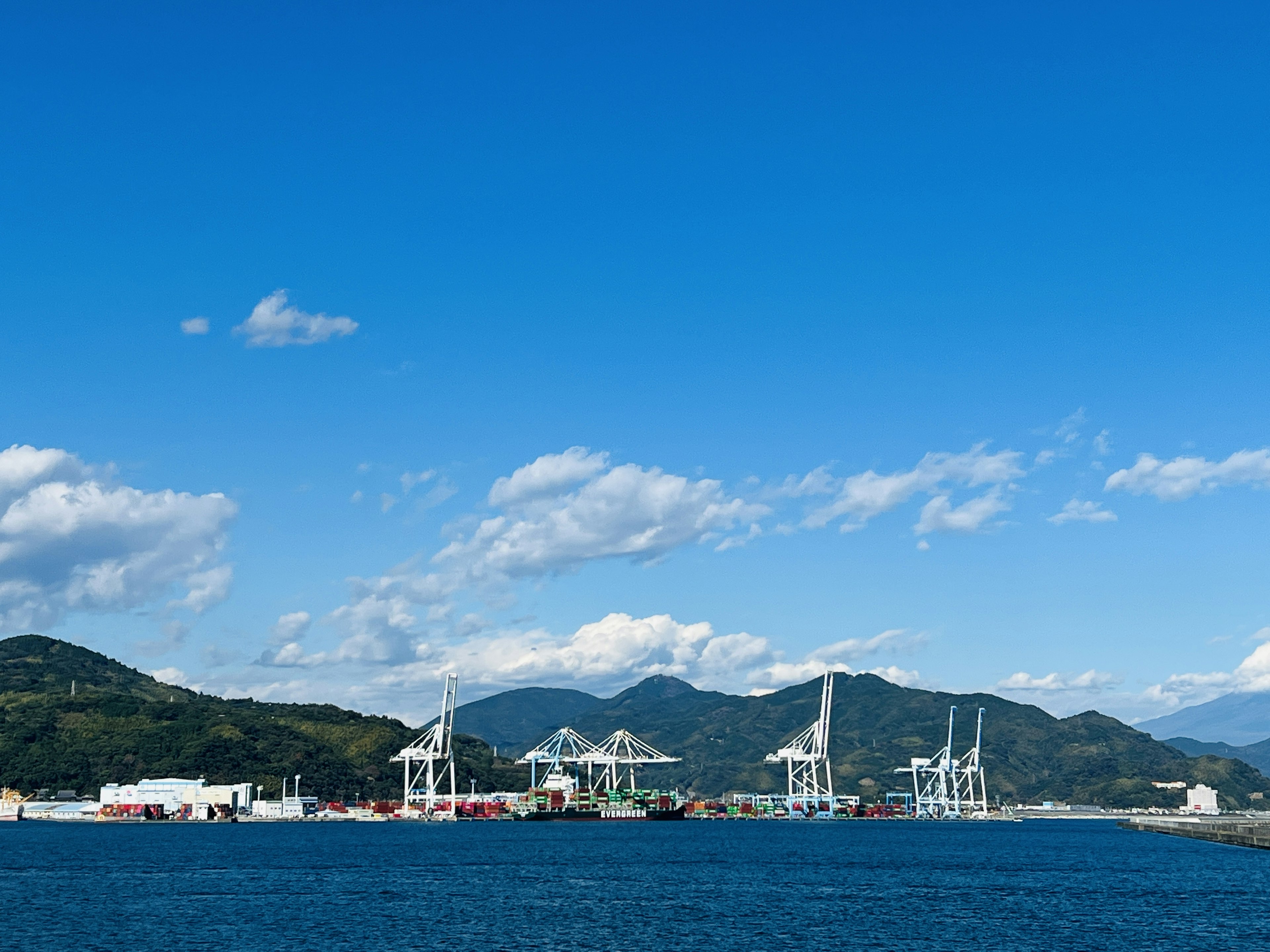 ทิวทัศน์ที่มีเครนในท่าเรือใต้ท้องฟ้าสีฟ้าพร้อมภูเขาในพื้นหลัง