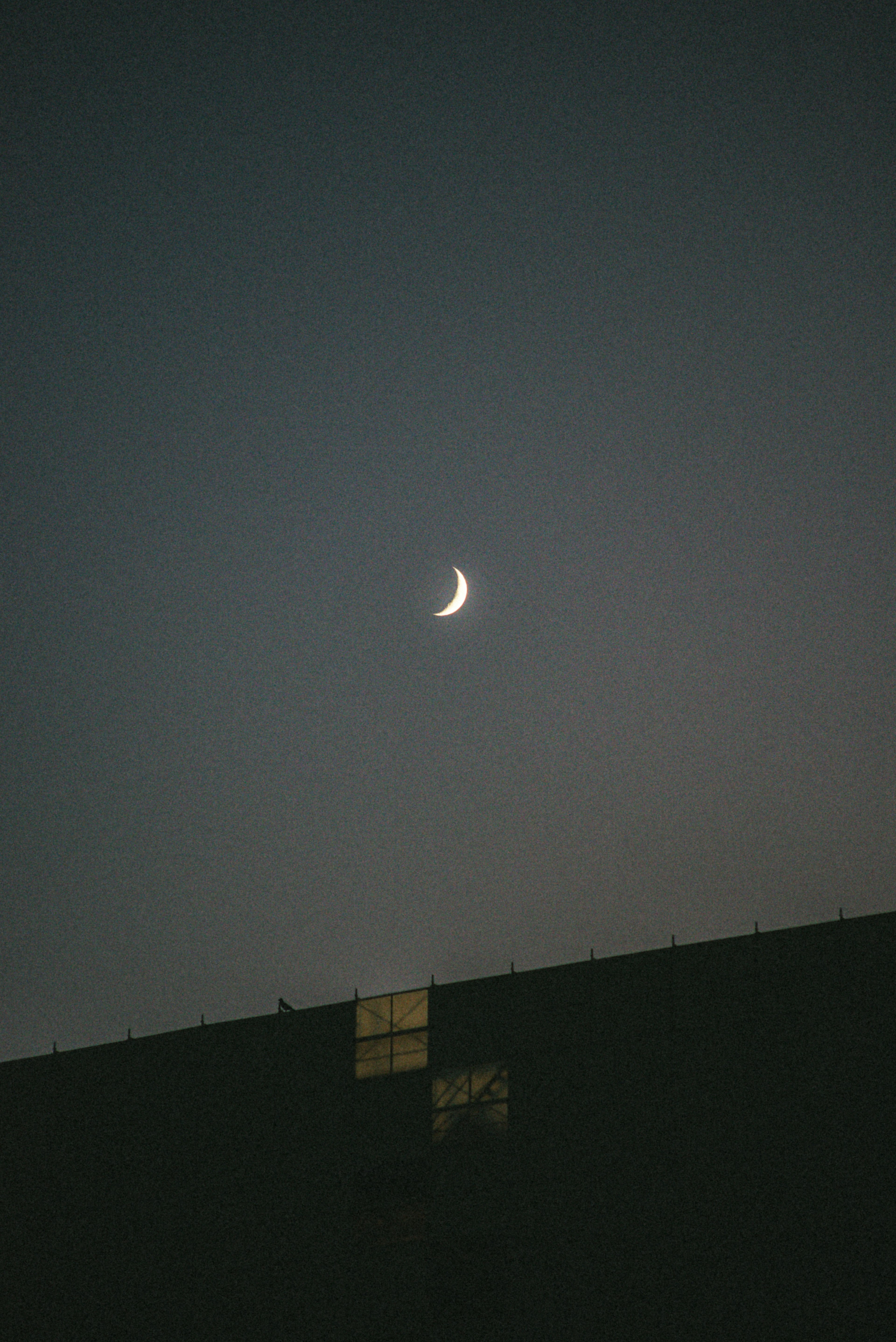 薄暗い夜空に浮かぶ細い三日月と建物のシルエット