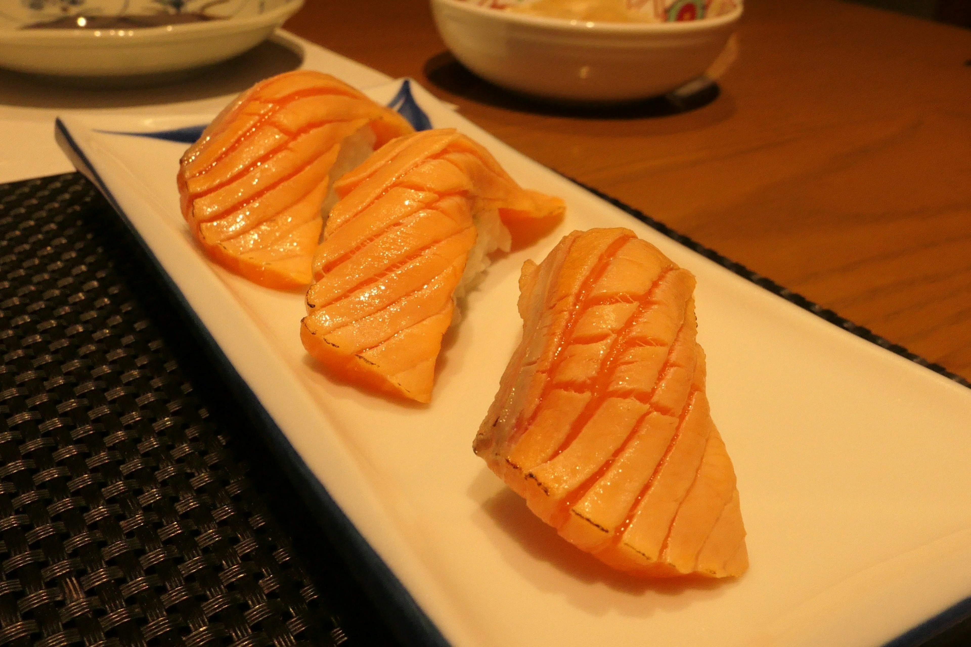 Three slices of salmon sashimi on a white plate