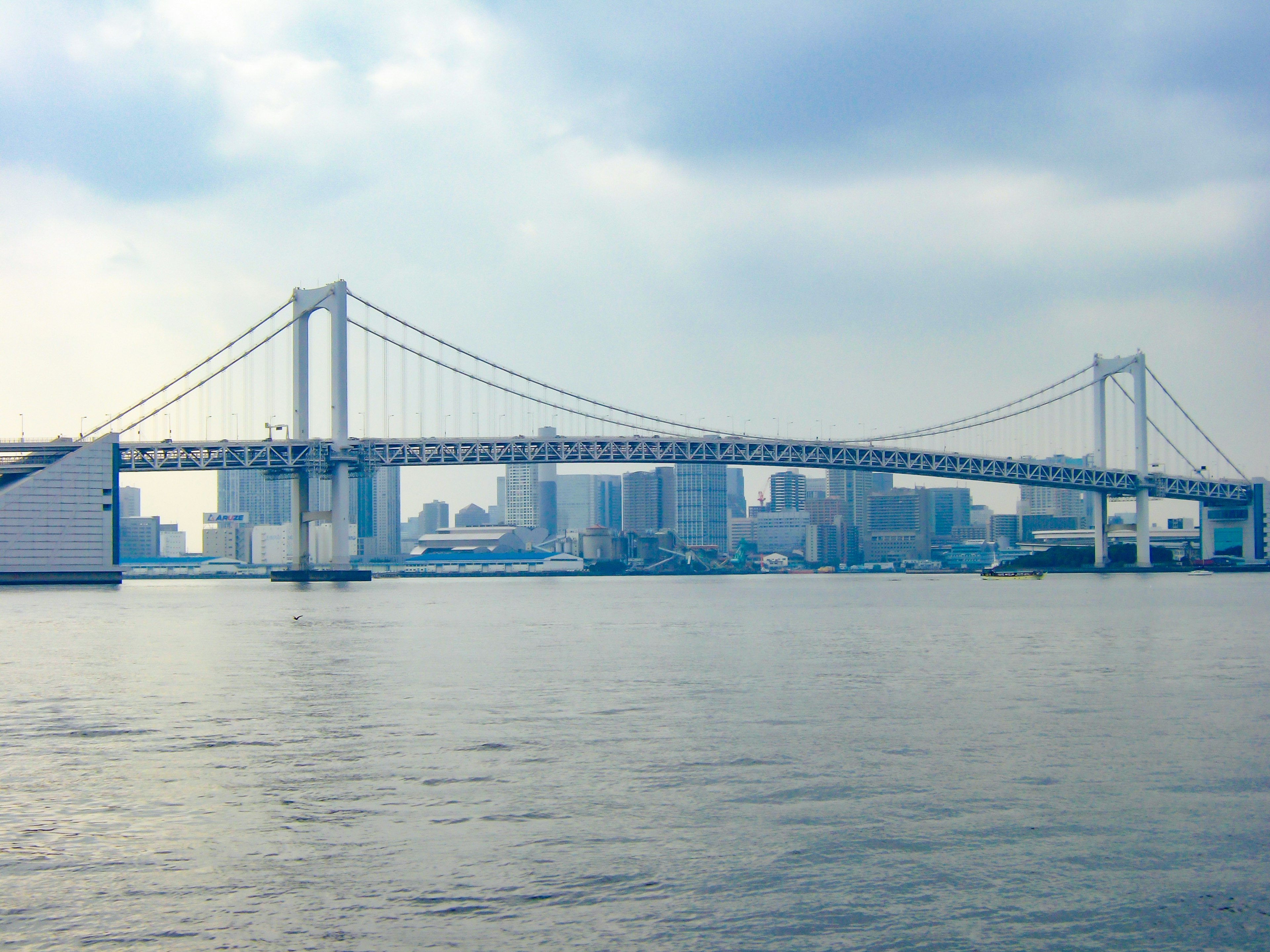 Blick auf die Rainbow Bridge mit der Skyline von Tokio im Hintergrund über ruhigem Wasser