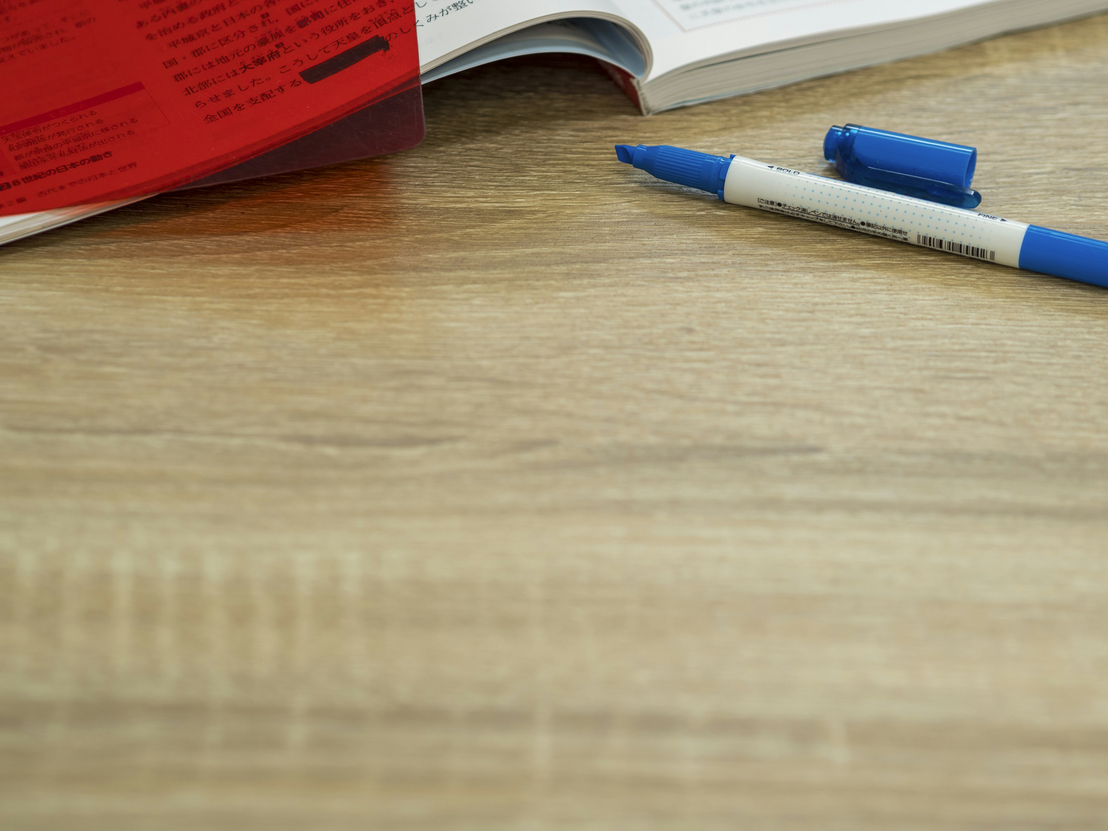 Livre rouge et stylos bleus sur une table en bois