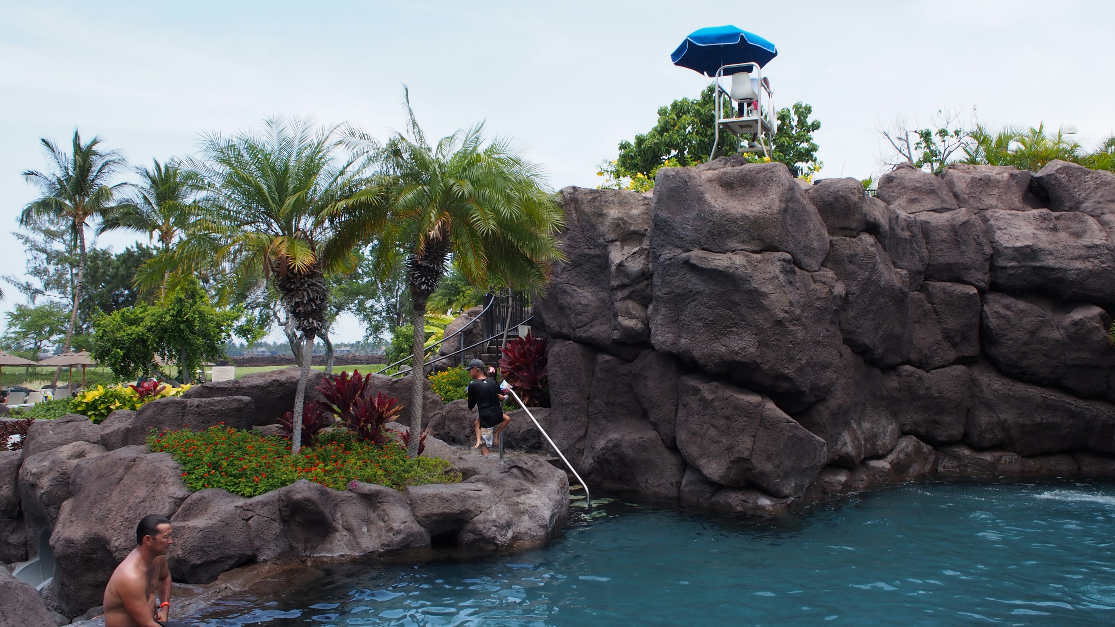 A scenic view of a pool area featuring a rocky ledge and a lifeguard tower