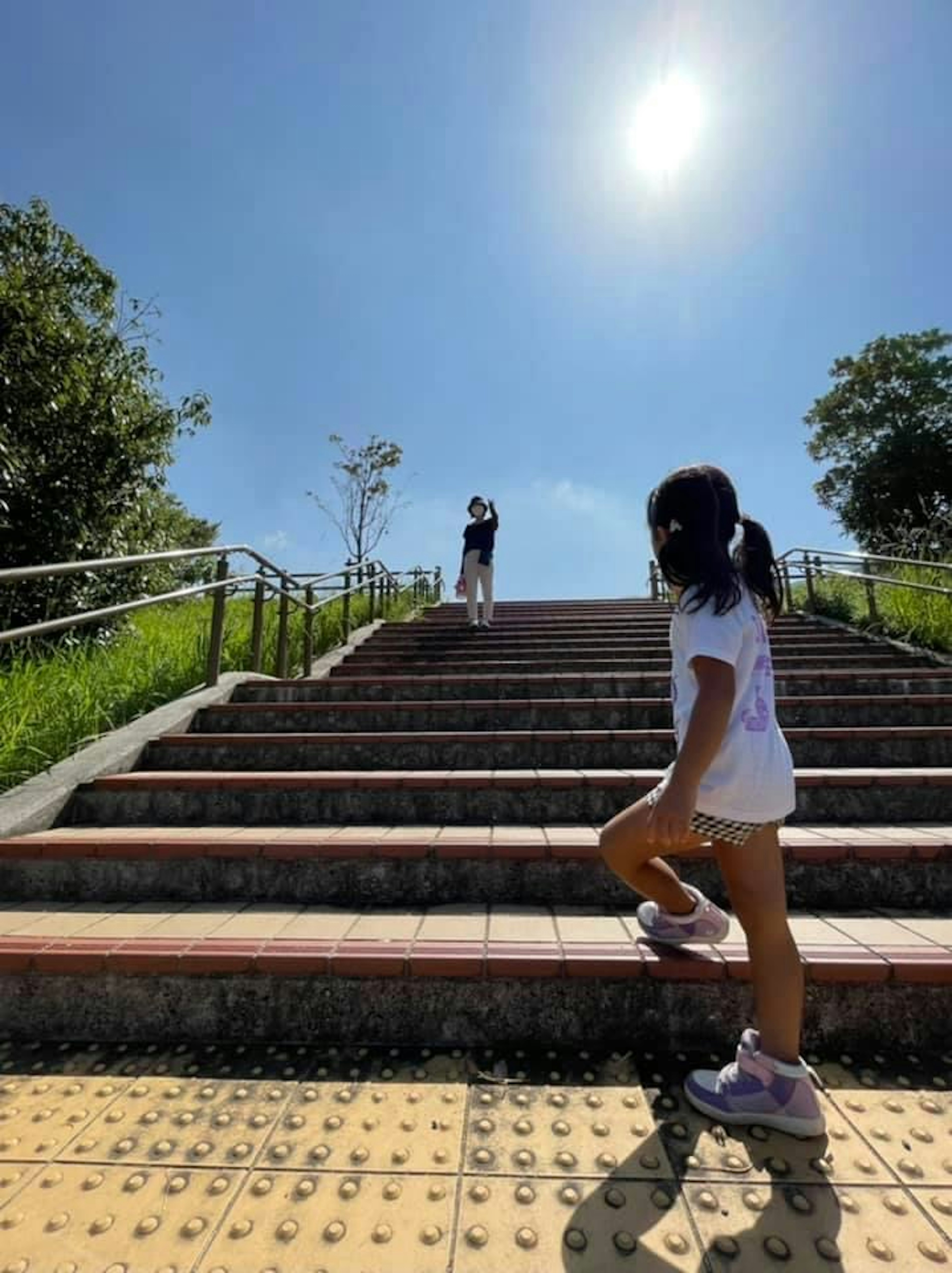 Child climbing stairs under a clear blue sky with an adult silhouette above