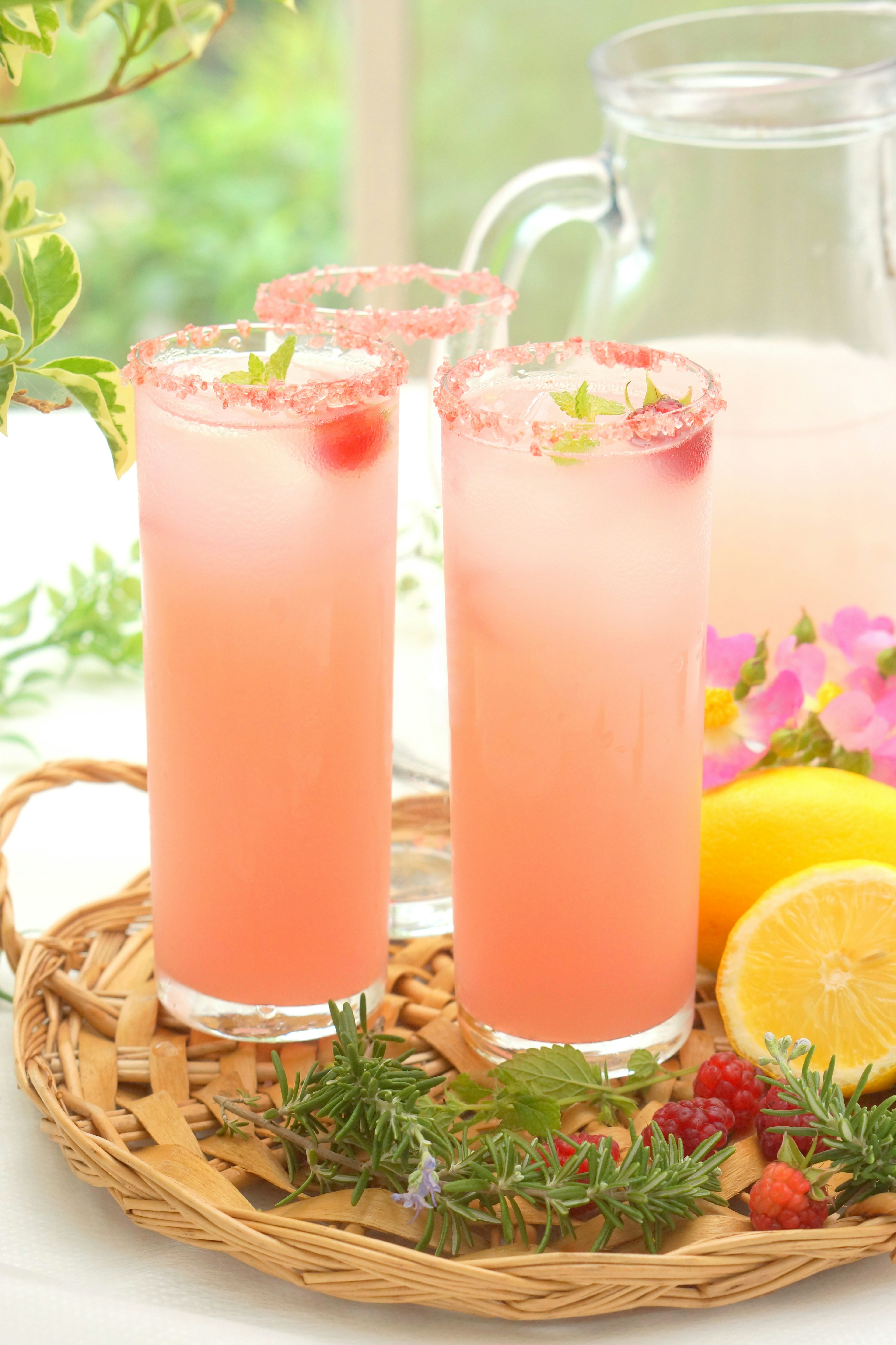 Two glasses of pink beverage on a tray with lemon and flowers in the background