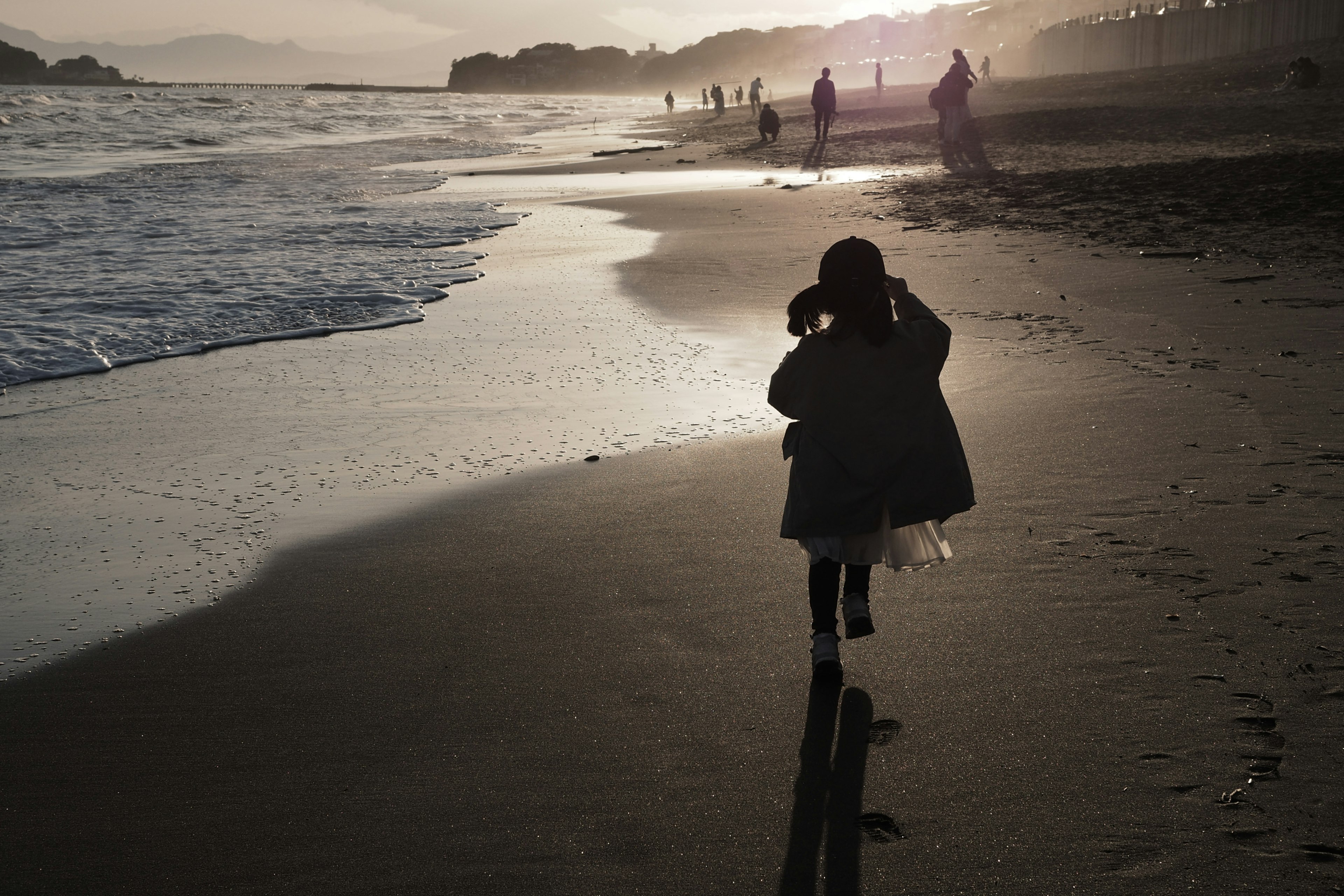 Silhouette di un bambino che cammina sulla spiaggia tramonto che illumina la sabbia