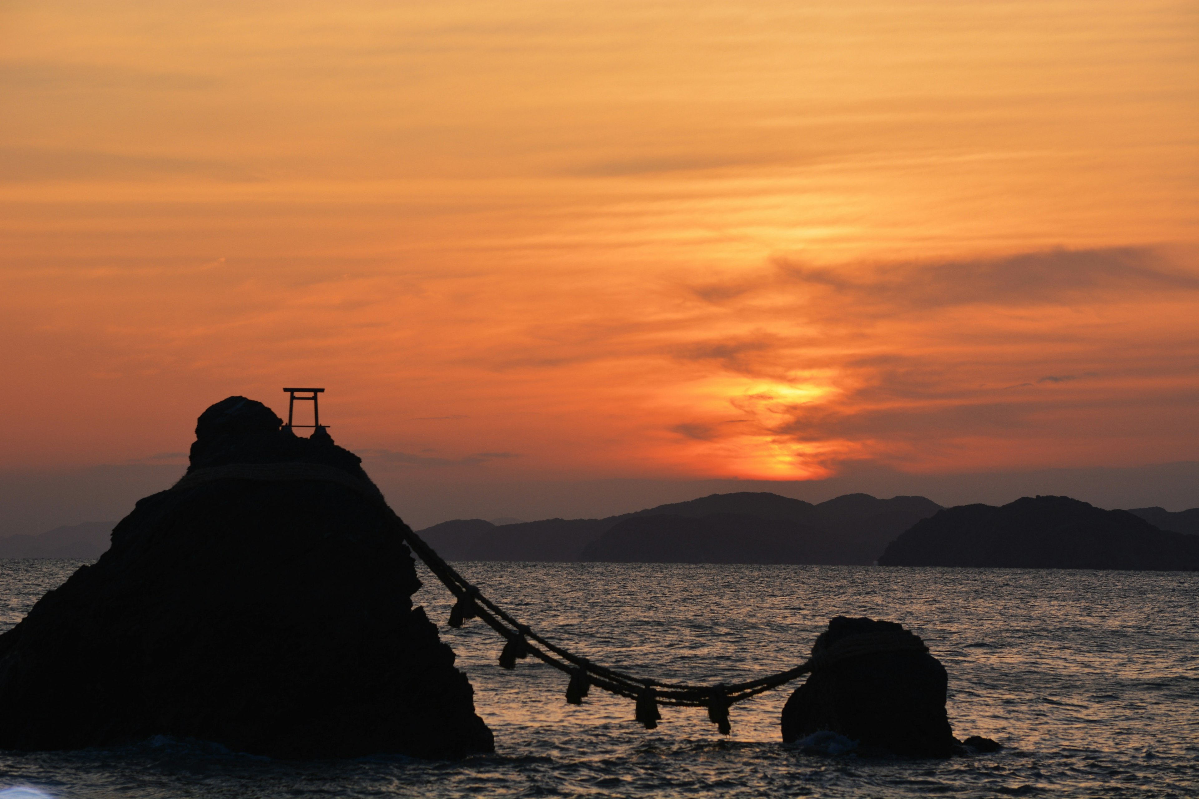 夕日が沈む海に浮かぶ岩とその間をつなぐ橋