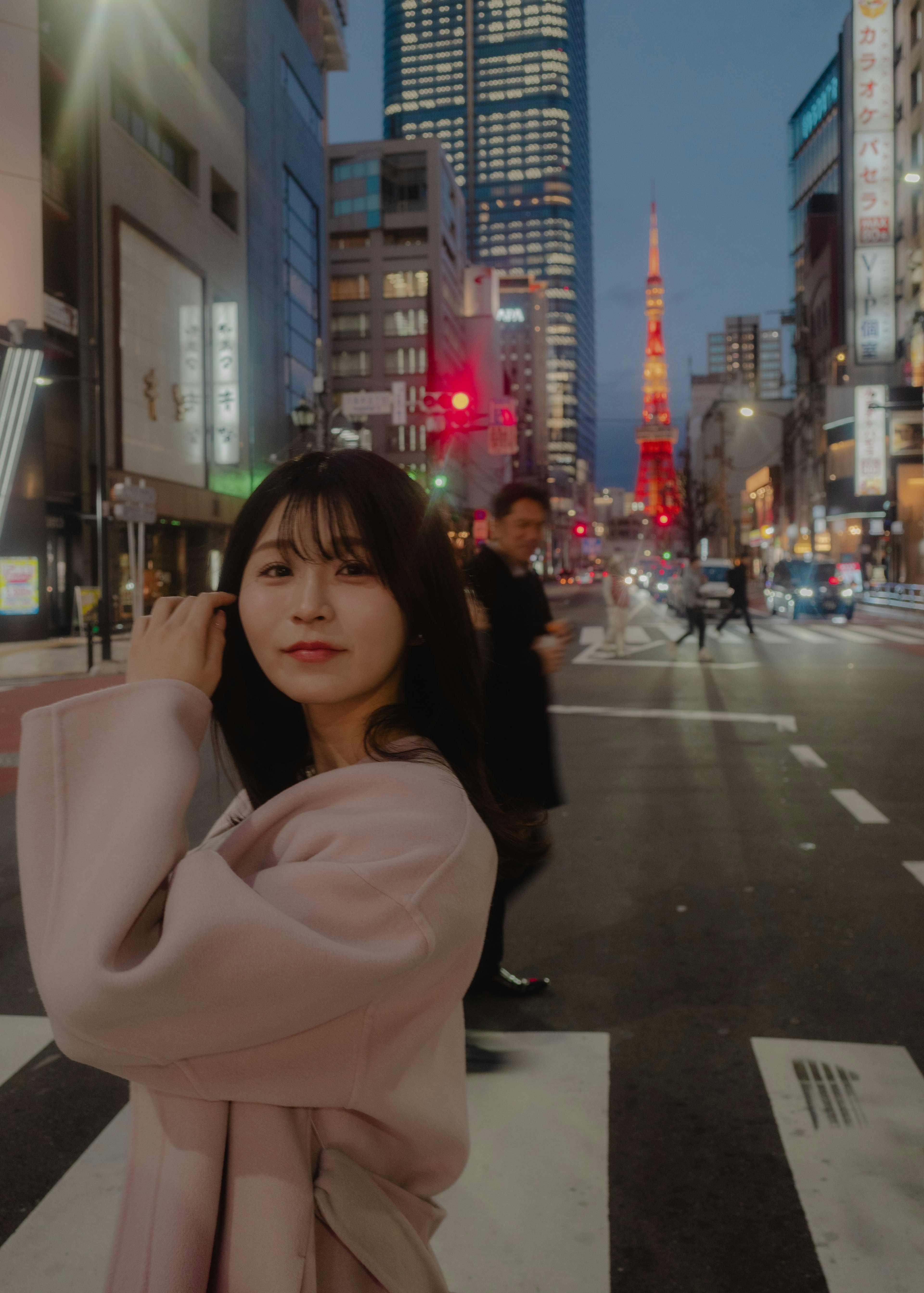 Une femme posant à un carrefour de Tokyo avec la tour de Tokyo illuminée en arrière-plan