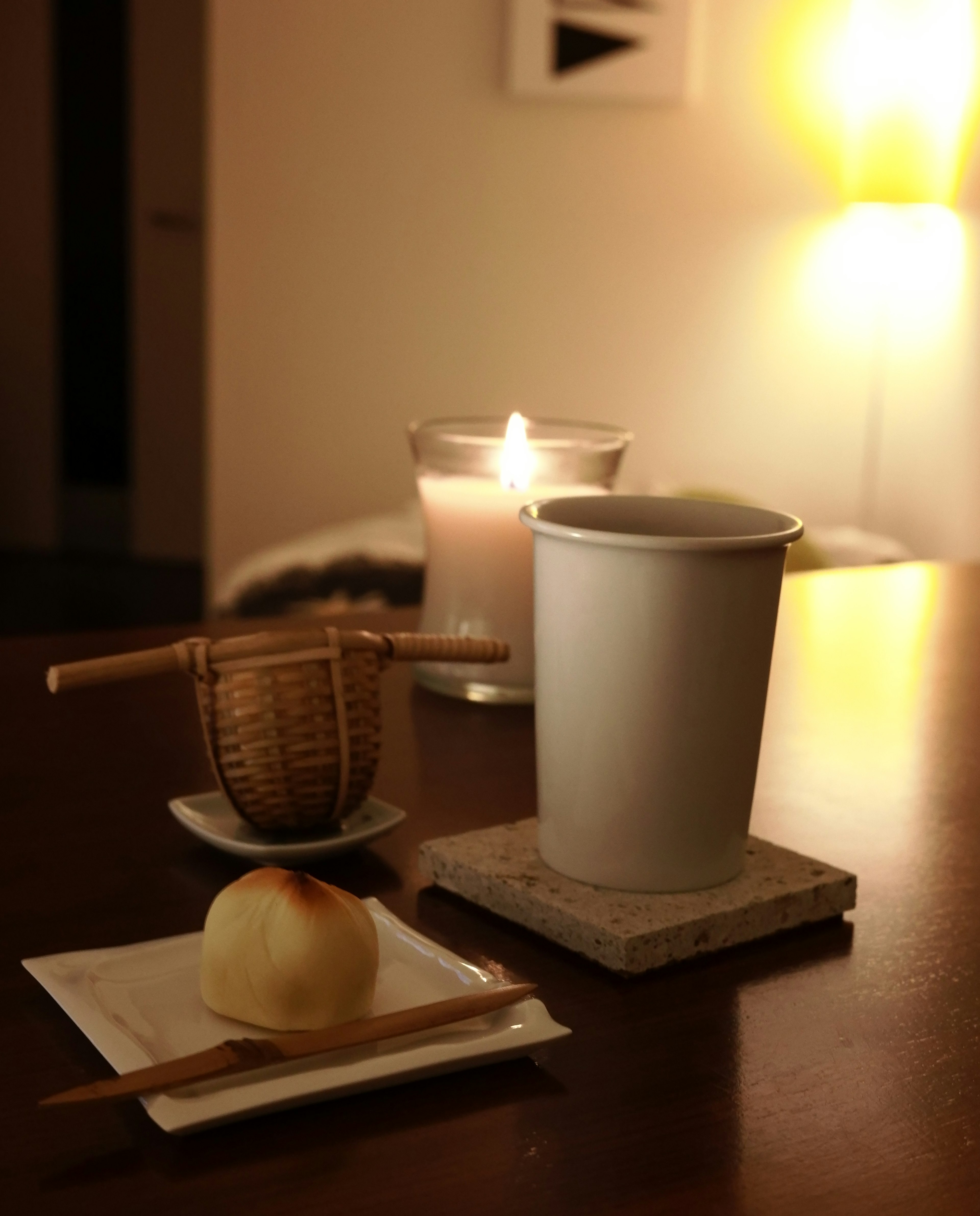 Una taza blanca y una vela sobre una mesa de madera con un dulce japonés