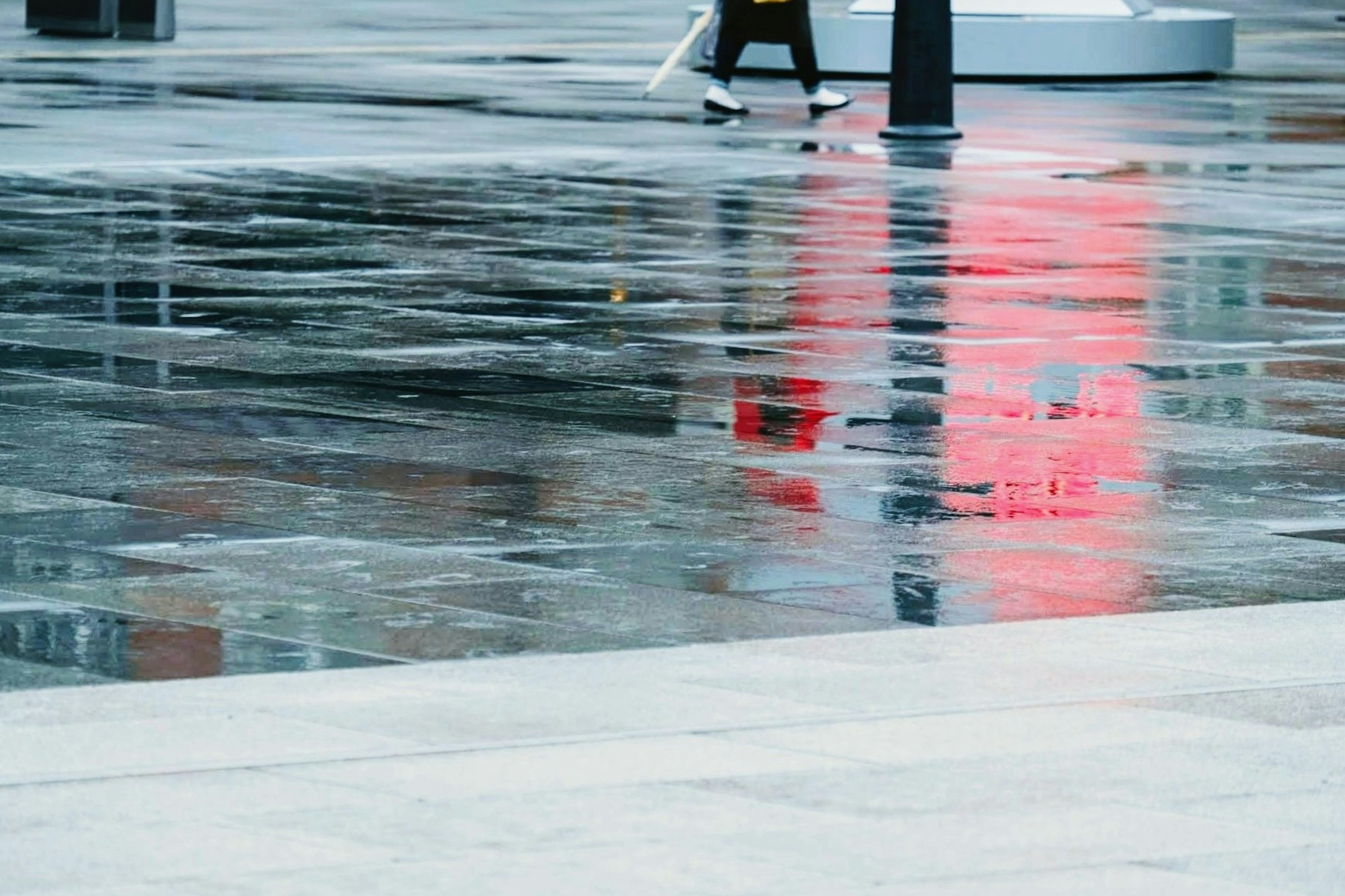 A person walking on a wet surface reflecting a red sign