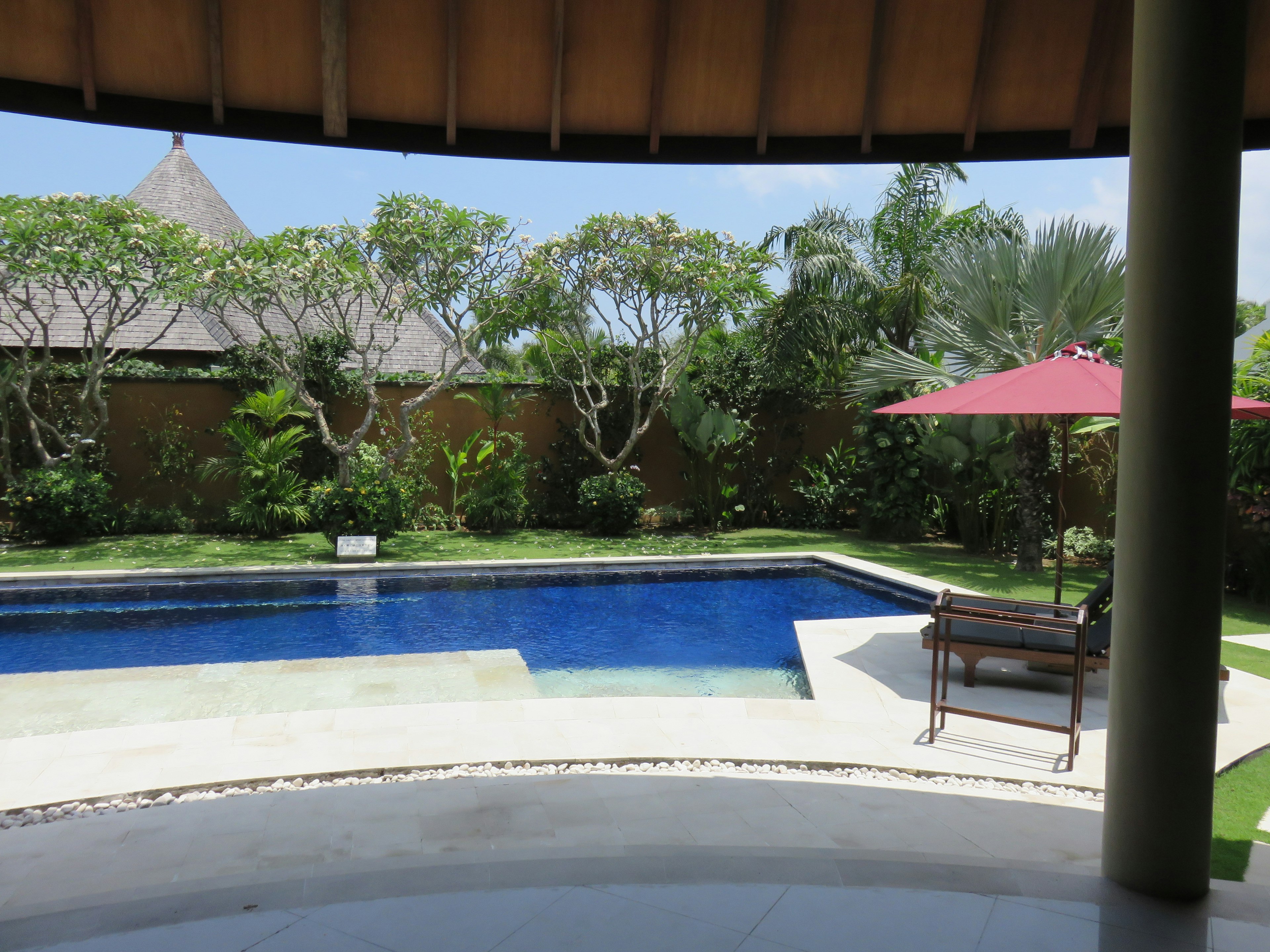 Schöner Blick auf einen Pool und einen grünen Garten mit einem Sonnenschirm und einer Bank in einem entspannenden Raum