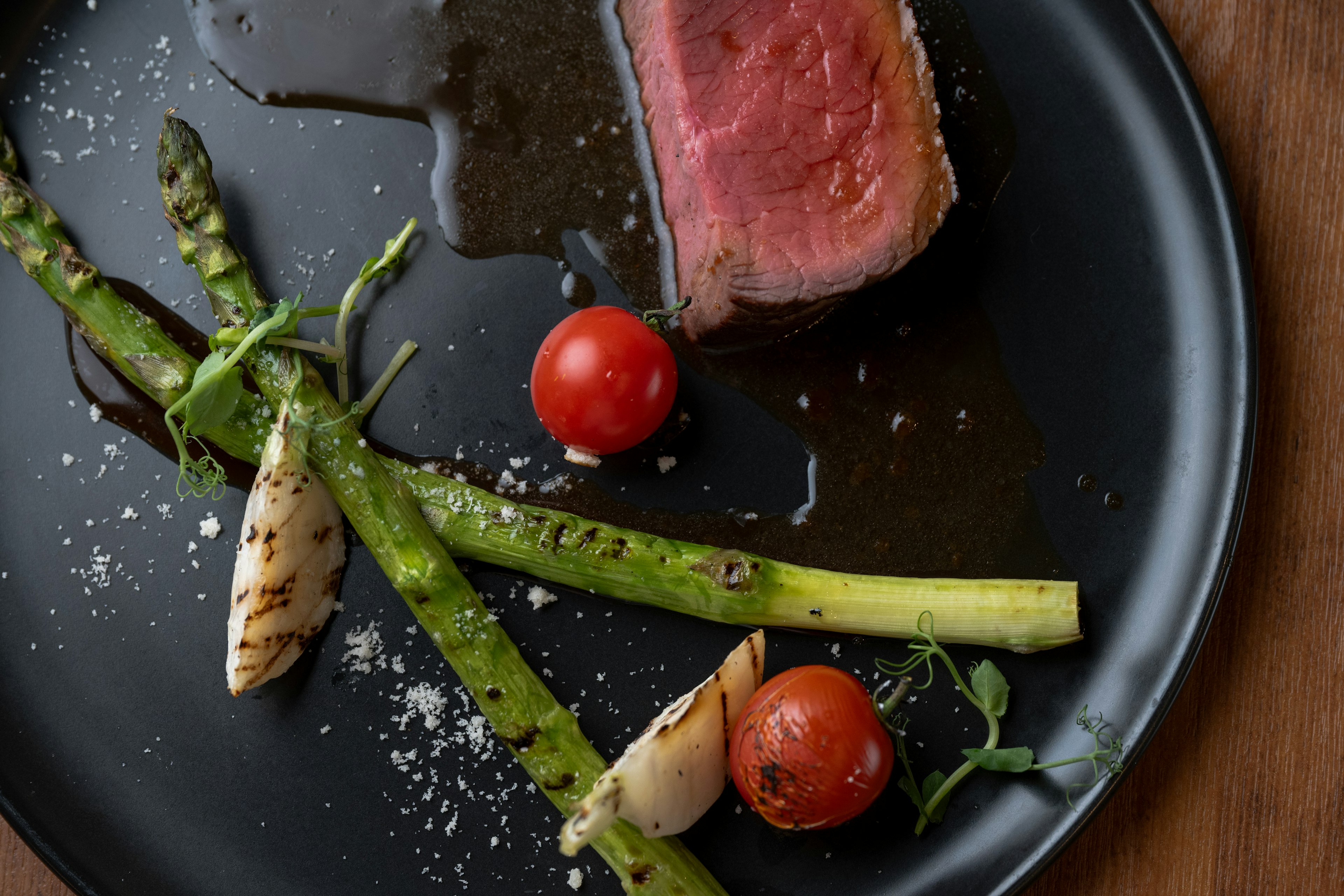 A perfectly cooked steak served on a black plate with asparagus and cherry tomatoes