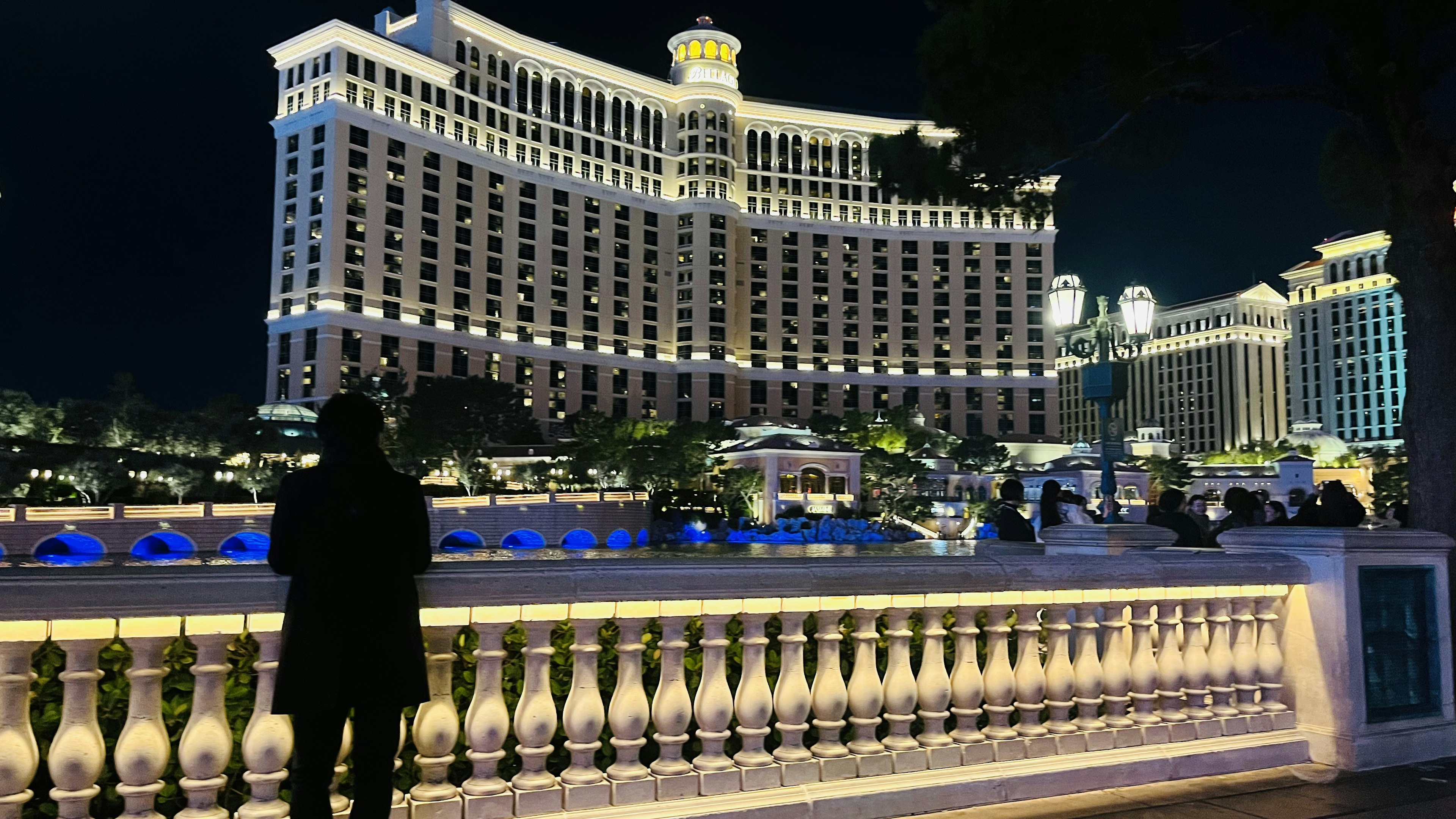 Person admiring the illuminated Bellagio Hotel and fountains at night