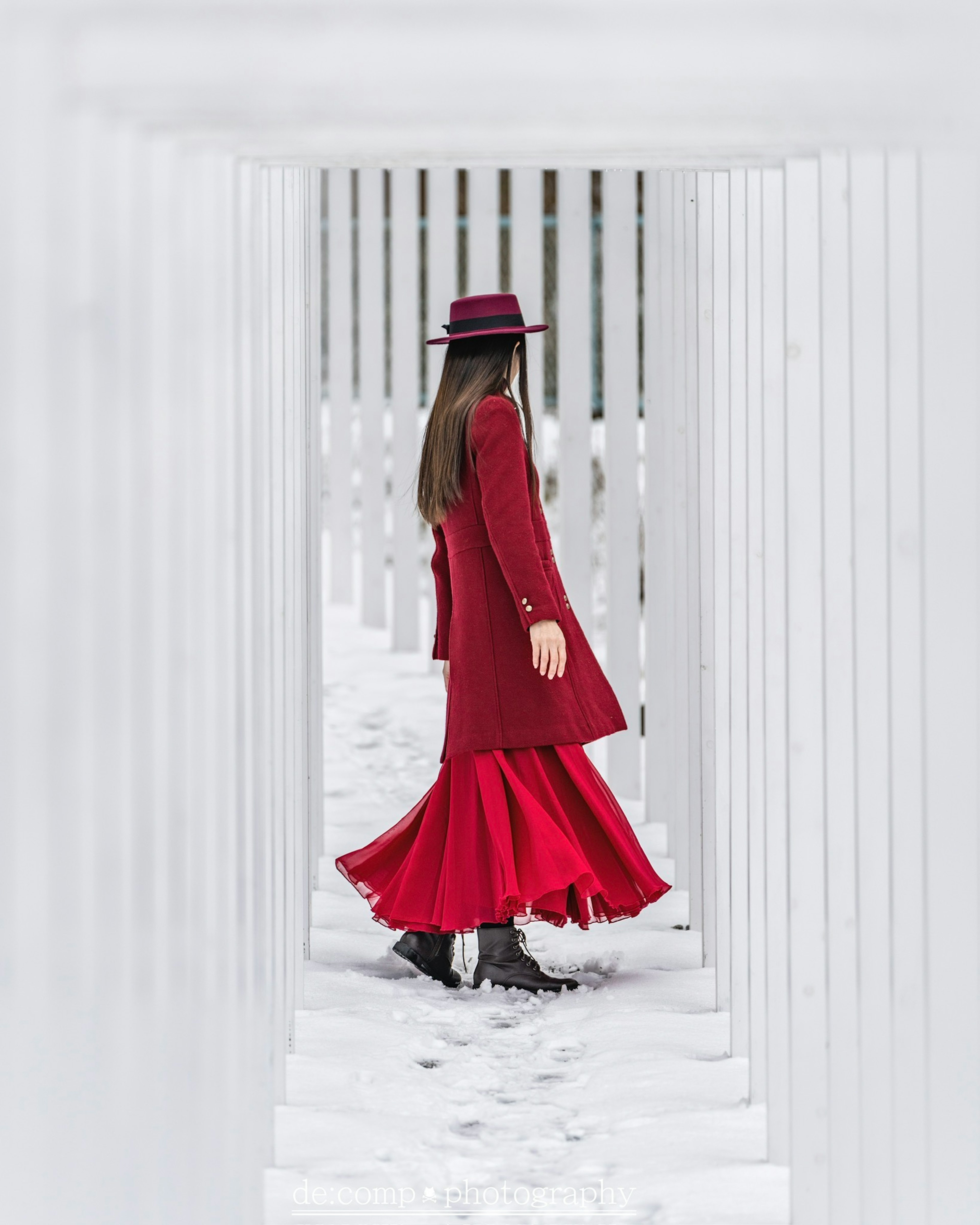 Una donna in abito rosso che cammina tra colonne bianche nella neve