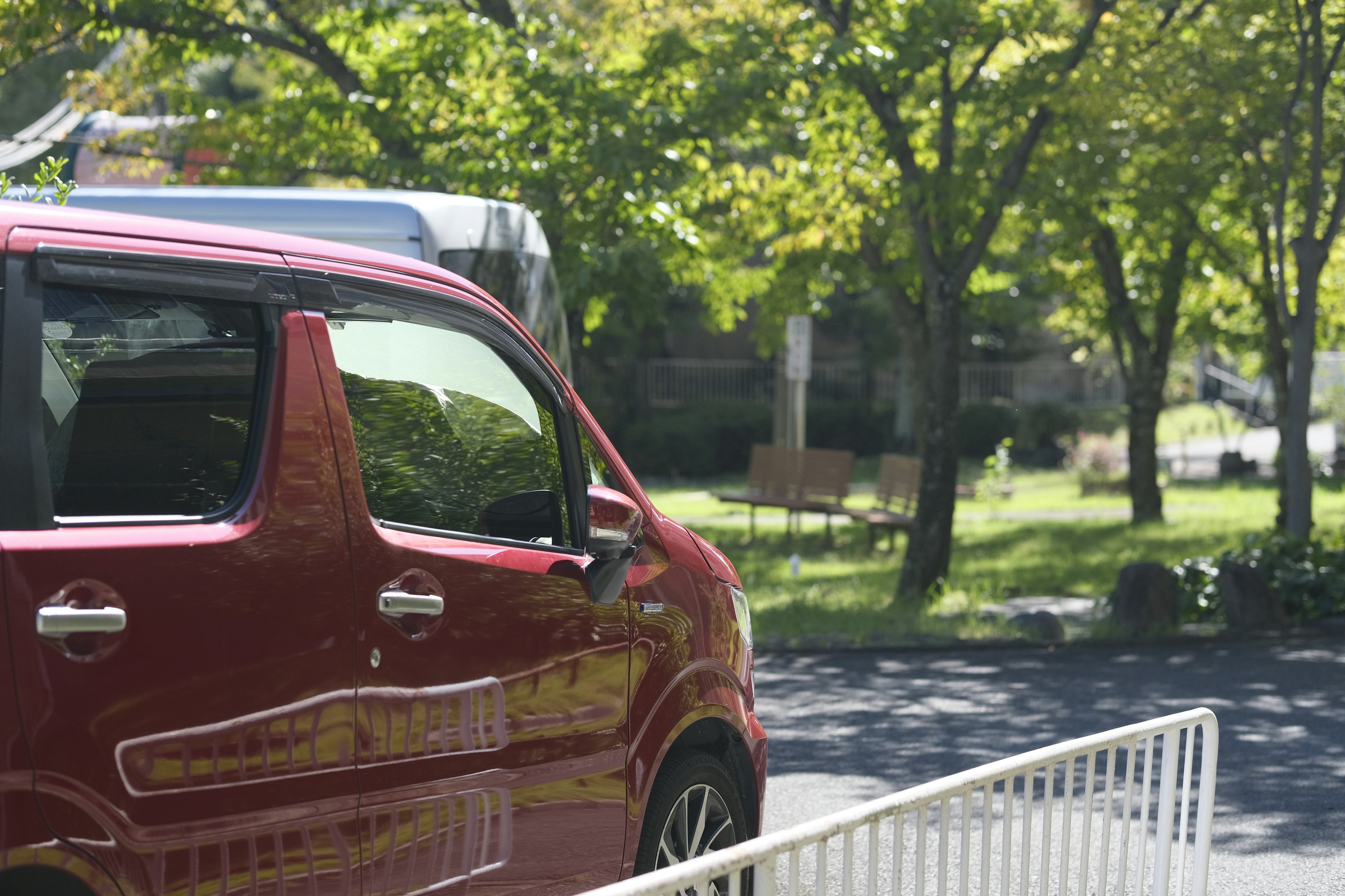 Auto rossa parcheggiata vicino a un parco con alberi verdi