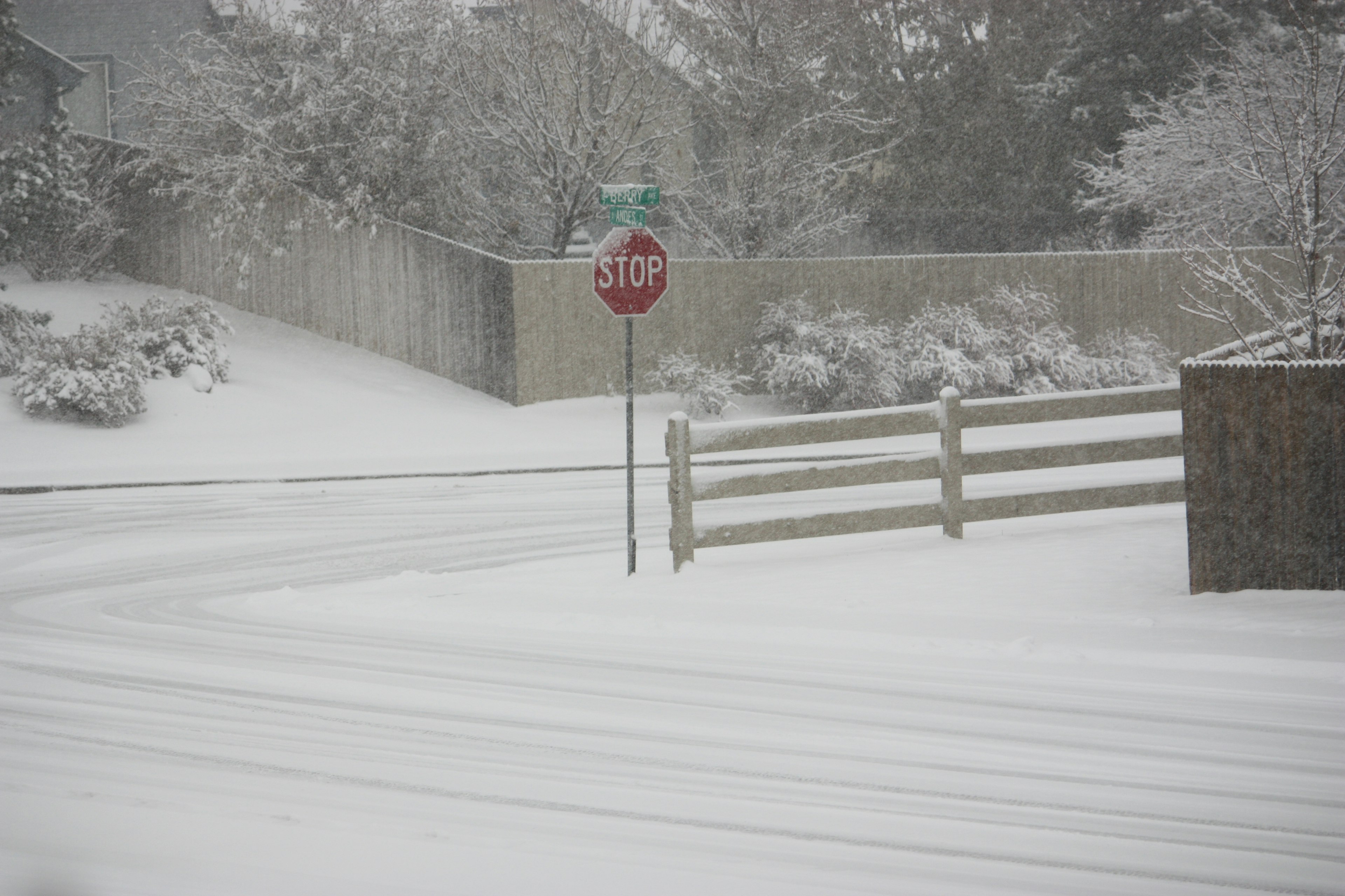 Snow-covered road with a stop sign and a wooden fence