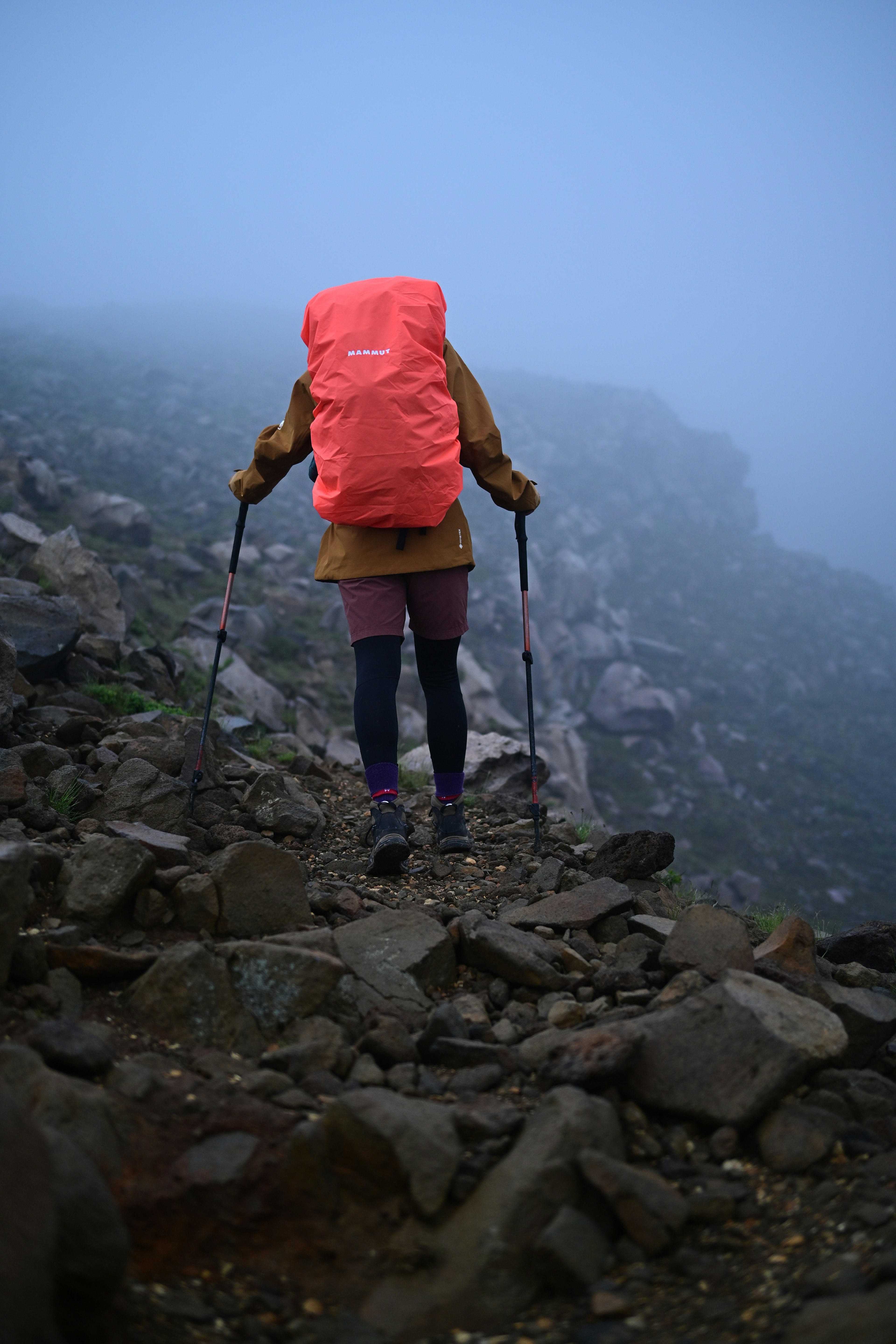 Wanderer mit einem orangefarbenen Rucksack, der auf einem felsigen Weg im Nebel geht