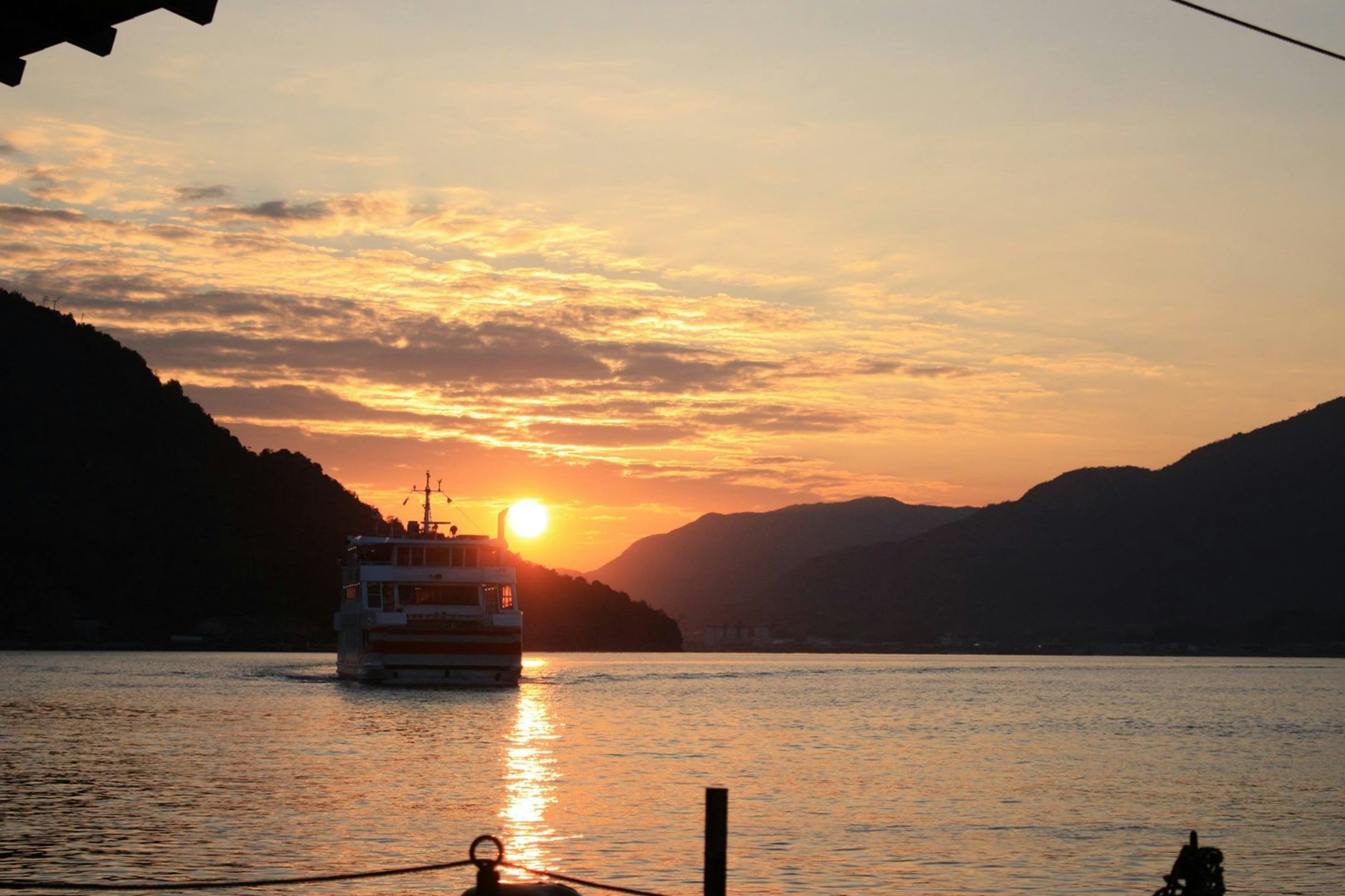 夕日が沈む山々と川を横切る船の風景