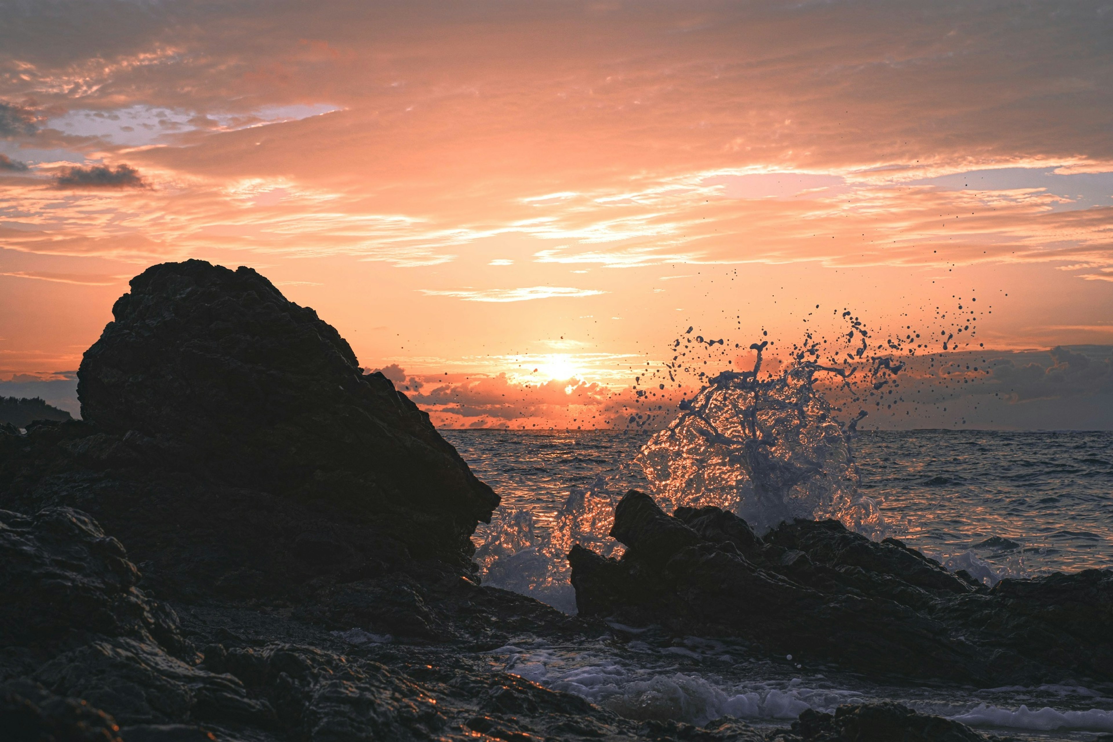 Waves crashing against rocks at sunset by the ocean