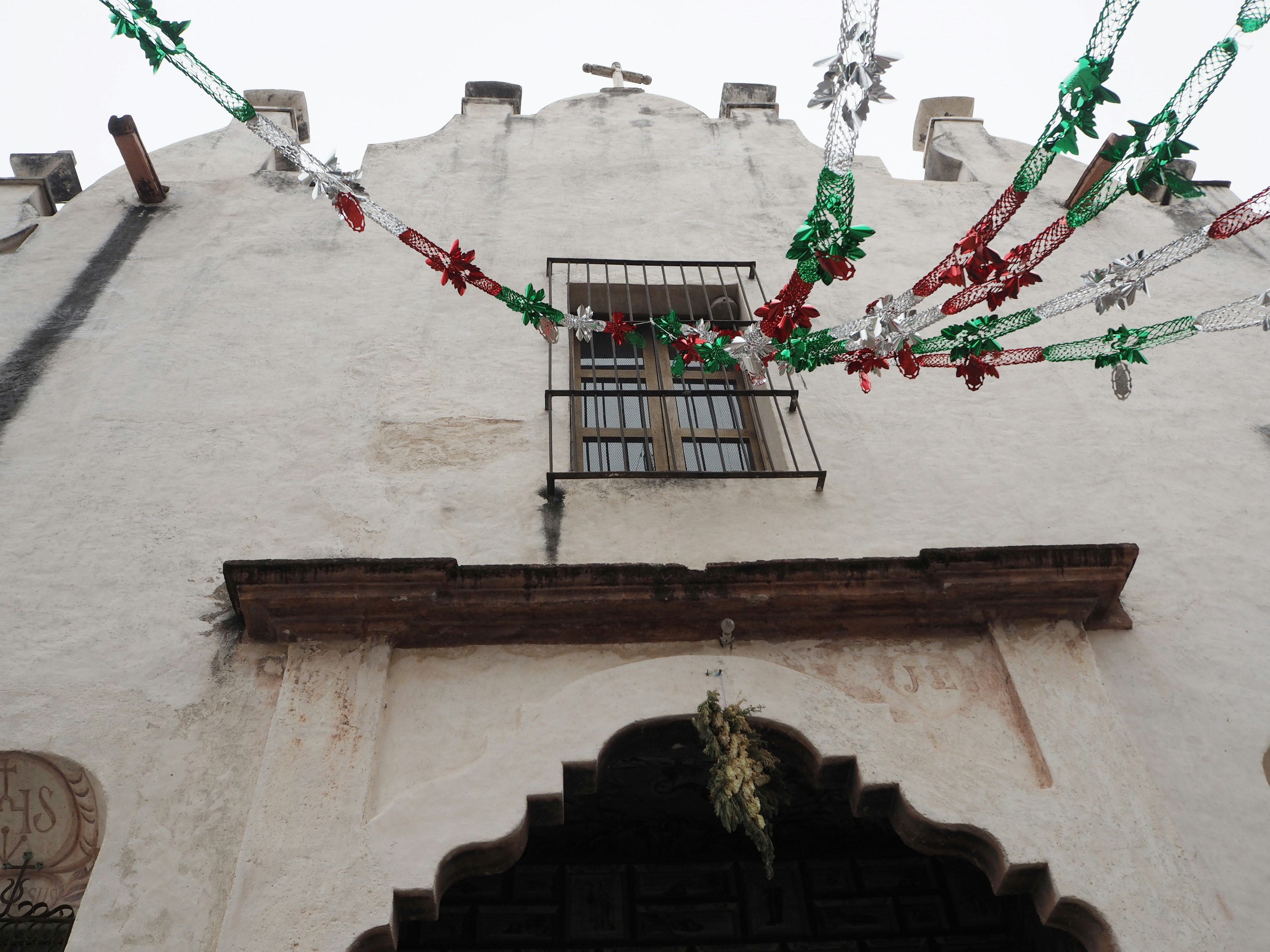 A white wall building with green and red decorations hanging above