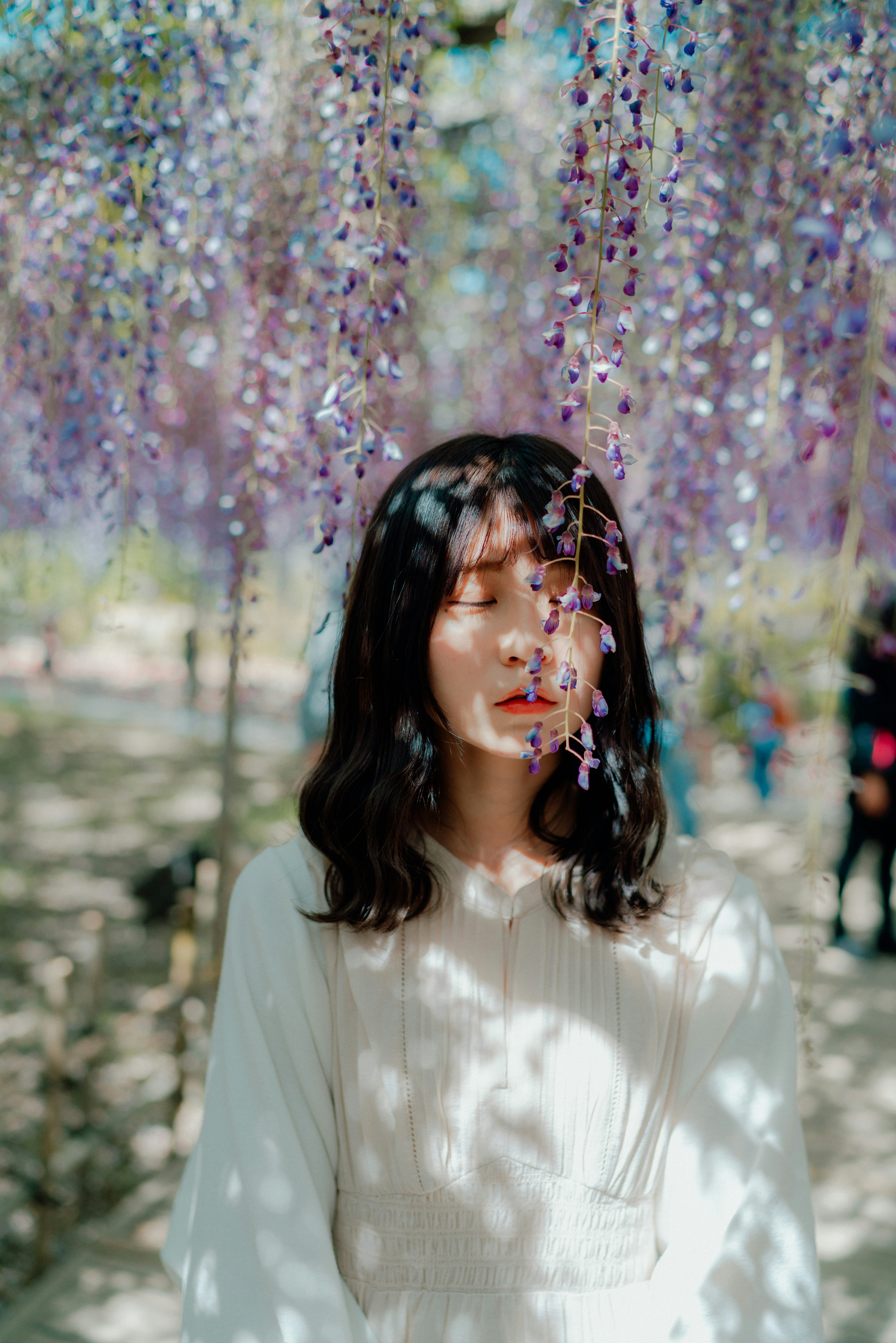 紫色の花が垂れ下がる中で微笑む女性のポートレート