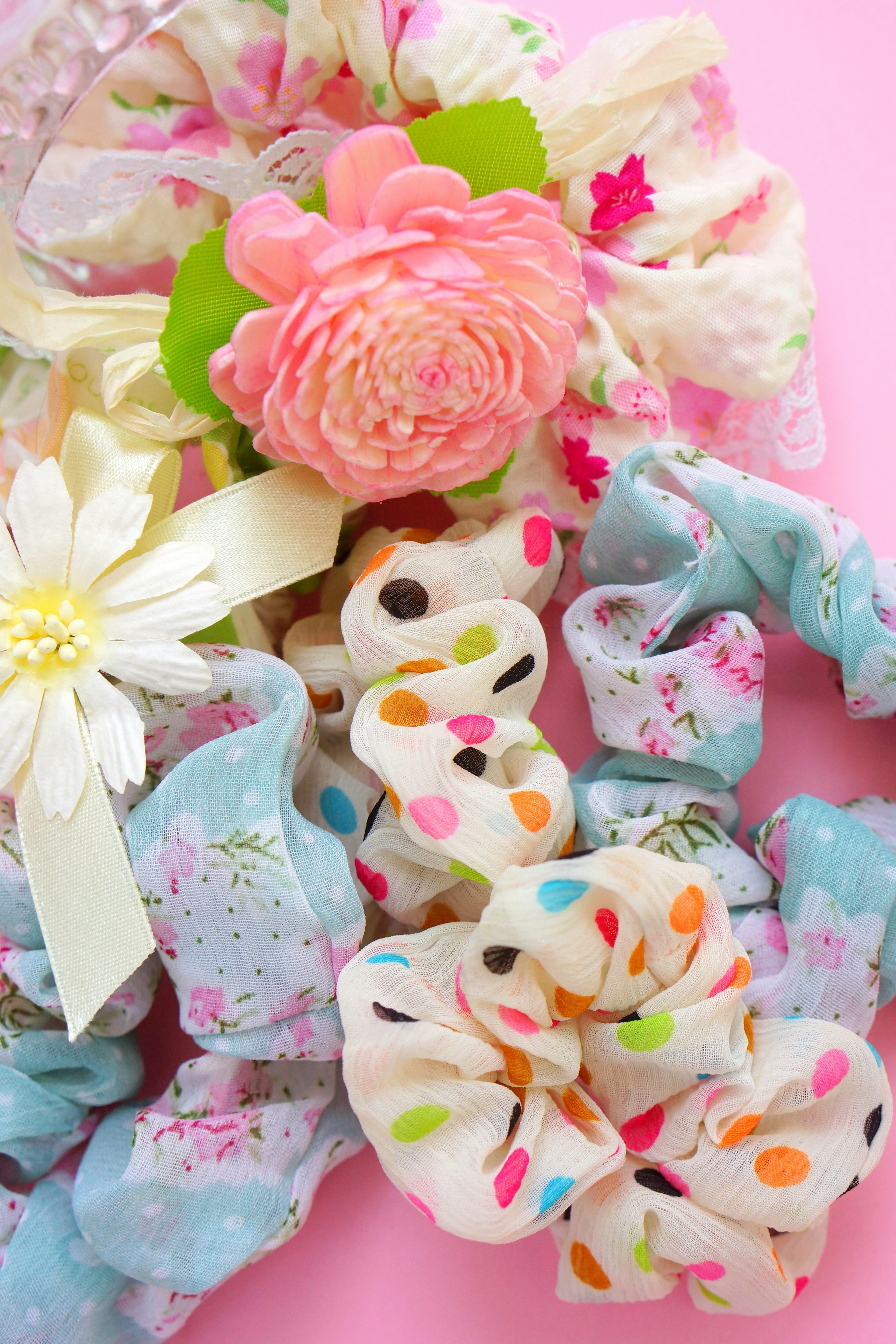 Colorful hair scrunchies and flower arrangement on a pink background