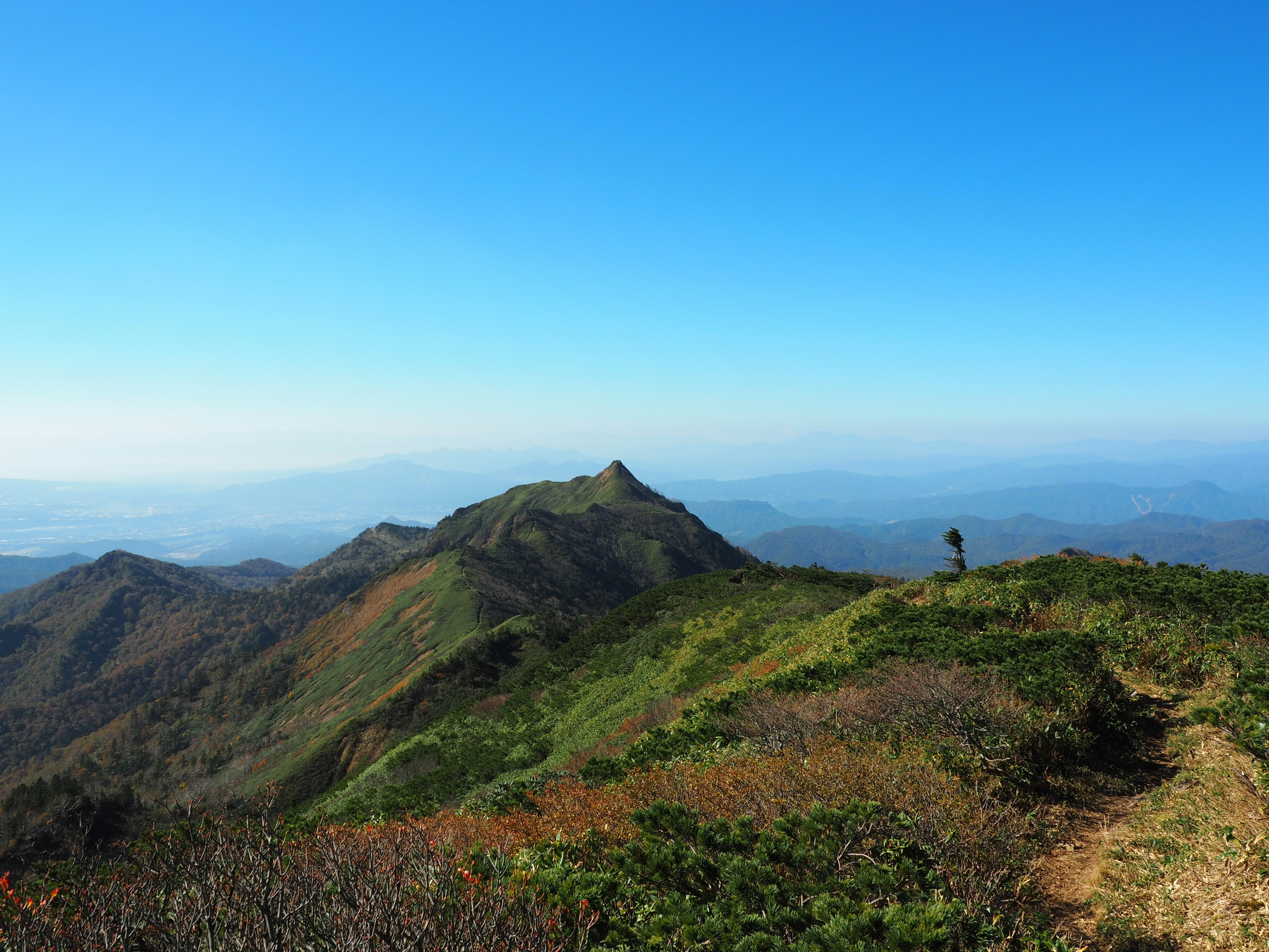 Pemandangan pegunungan di bawah langit biru pendaki melihat bukit hijau dan puncak jauh