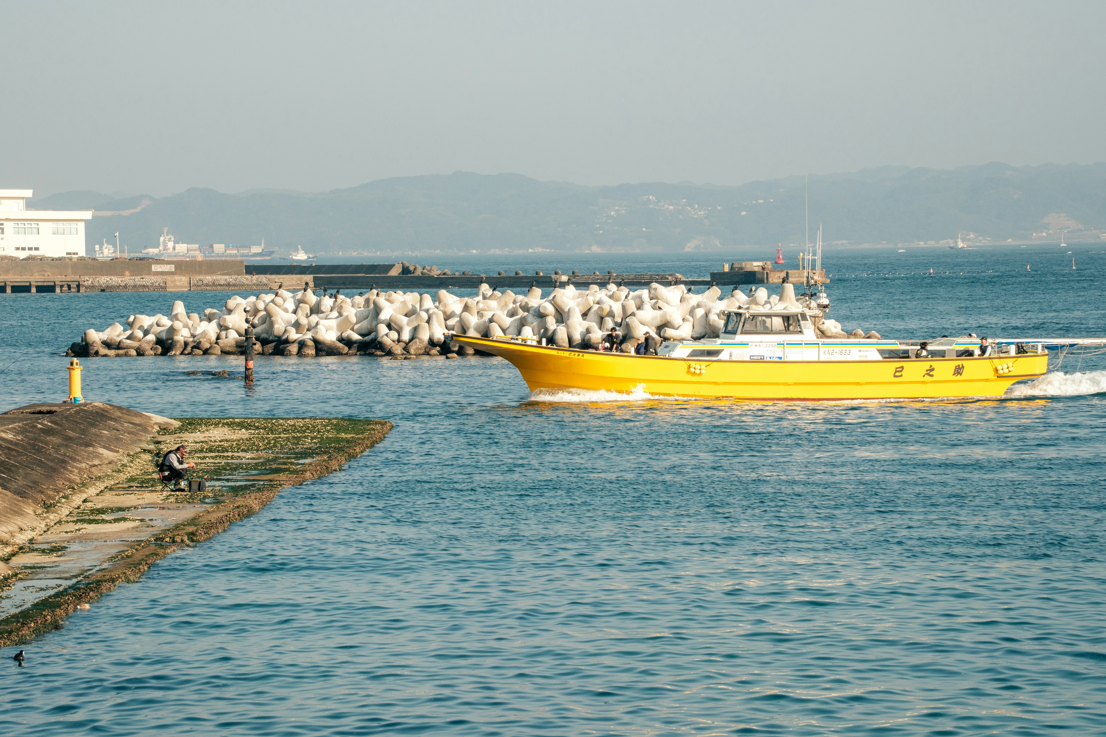 Barco amarillo navegando por el agua con un rompeolas rocoso al fondo