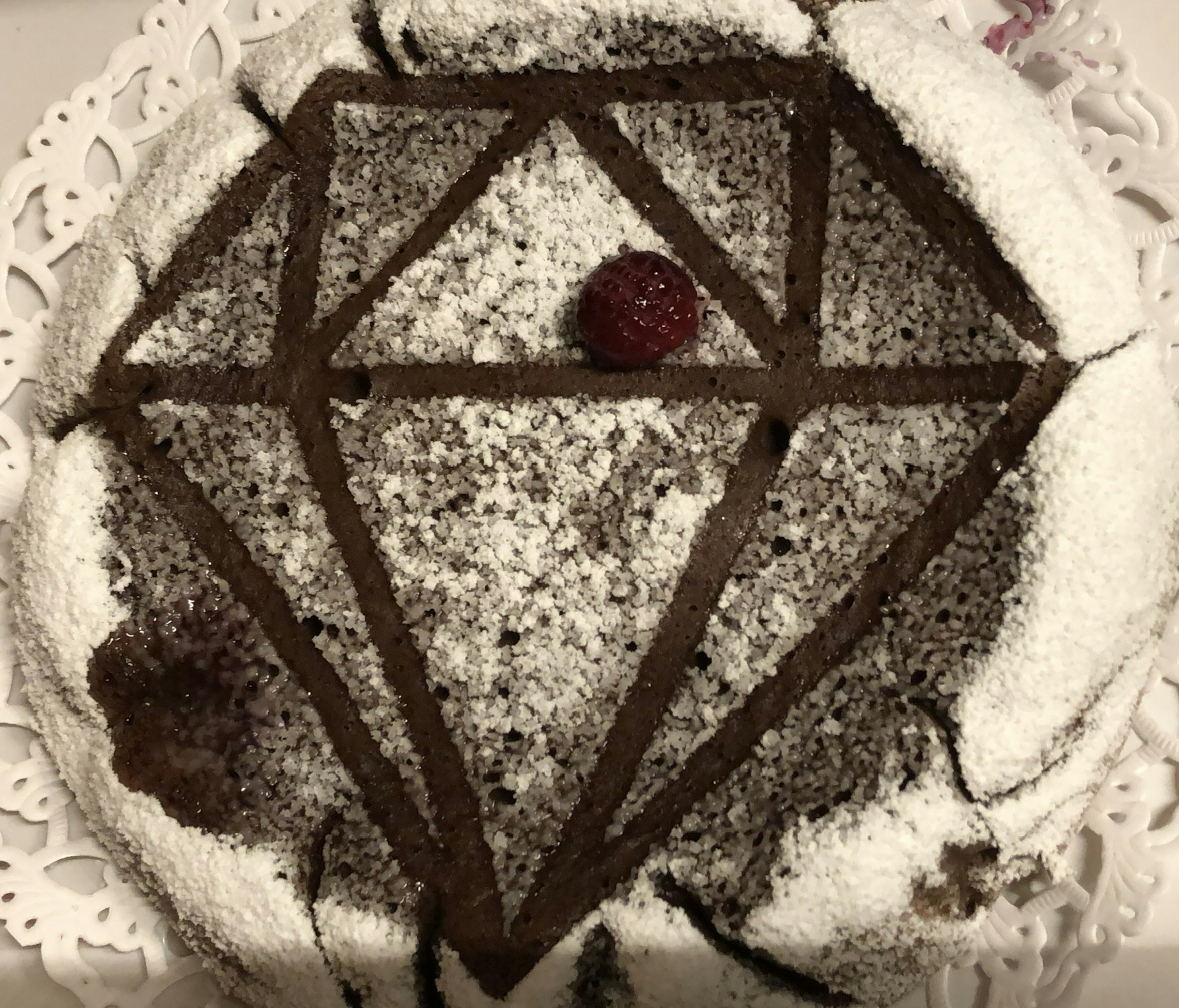 Chocolate cake shaped like a diamond with powdered sugar and a raspberry on top