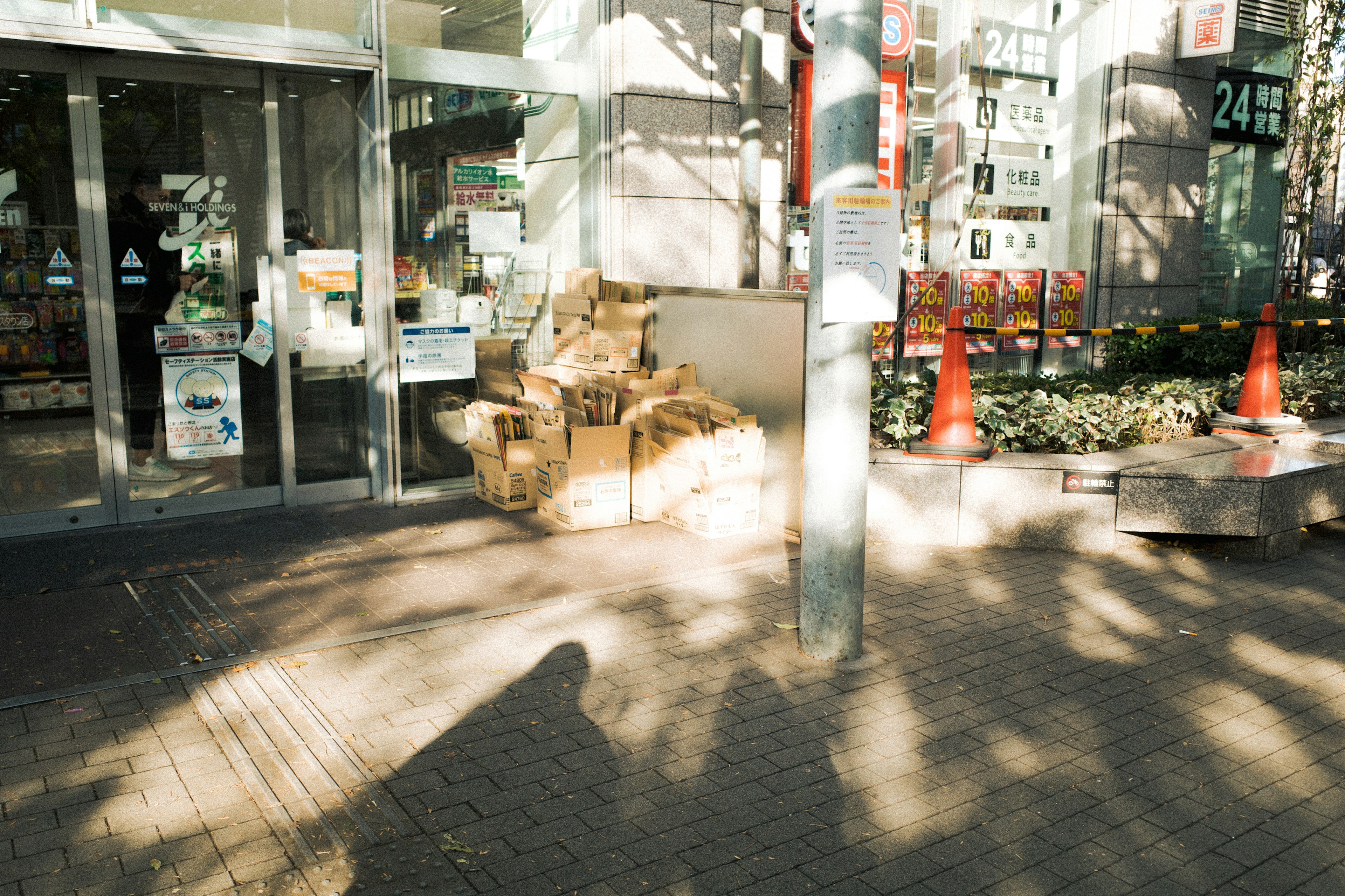 店舗の前に置かれた段ボールの山とオレンジのコーンが映る風景