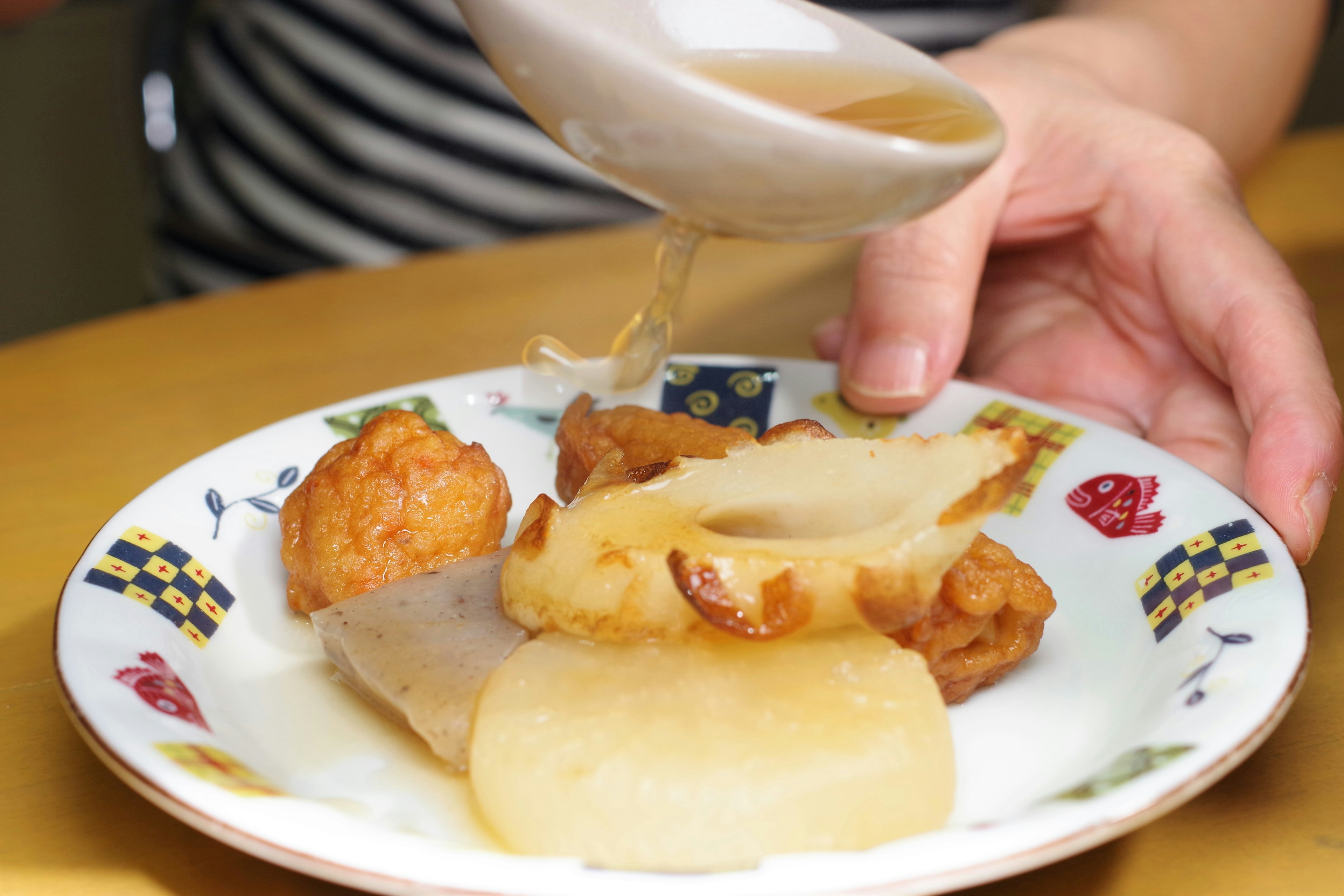 A hand pouring sauce over a plate of assorted simmered and fried dishes