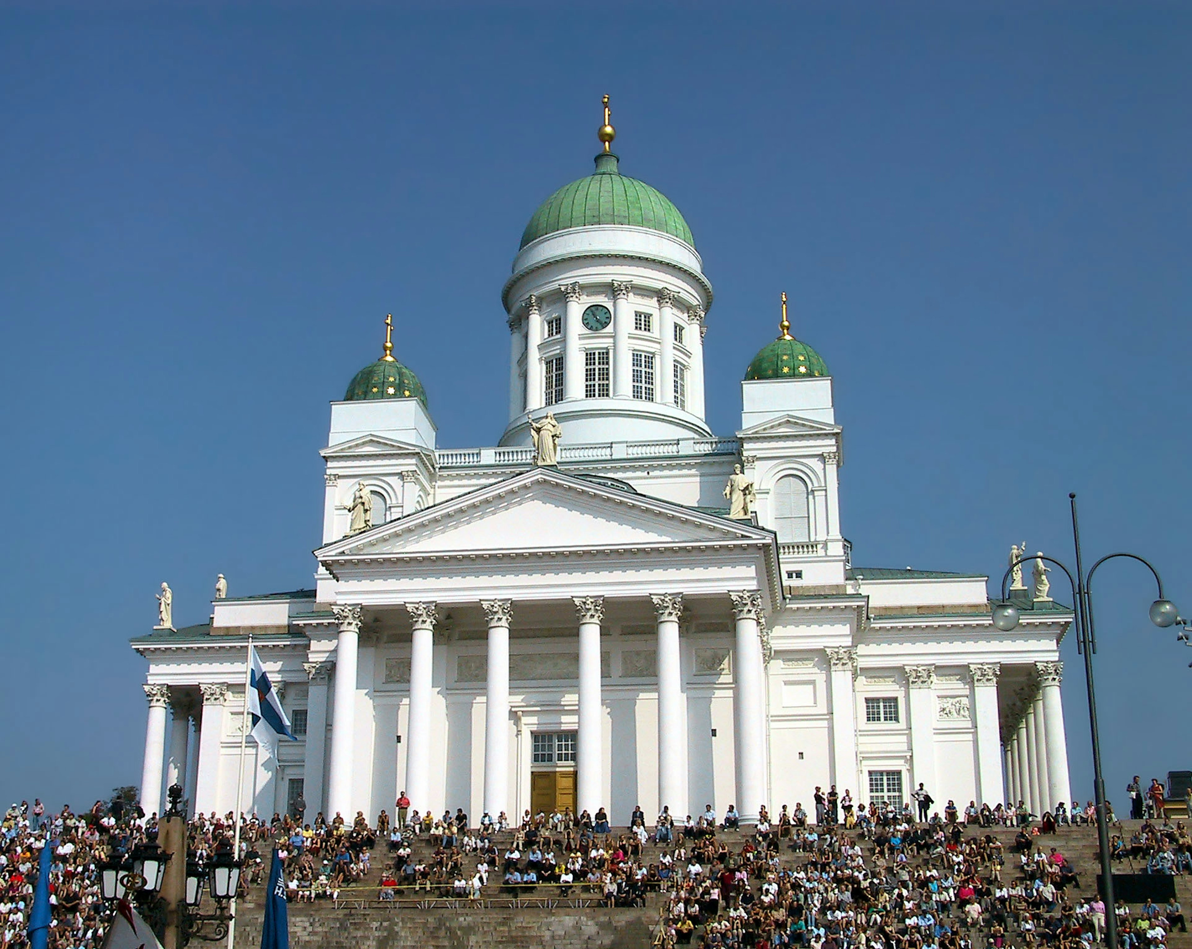 Helsinki Cathedral with white facade and green domes featuring a large crowd