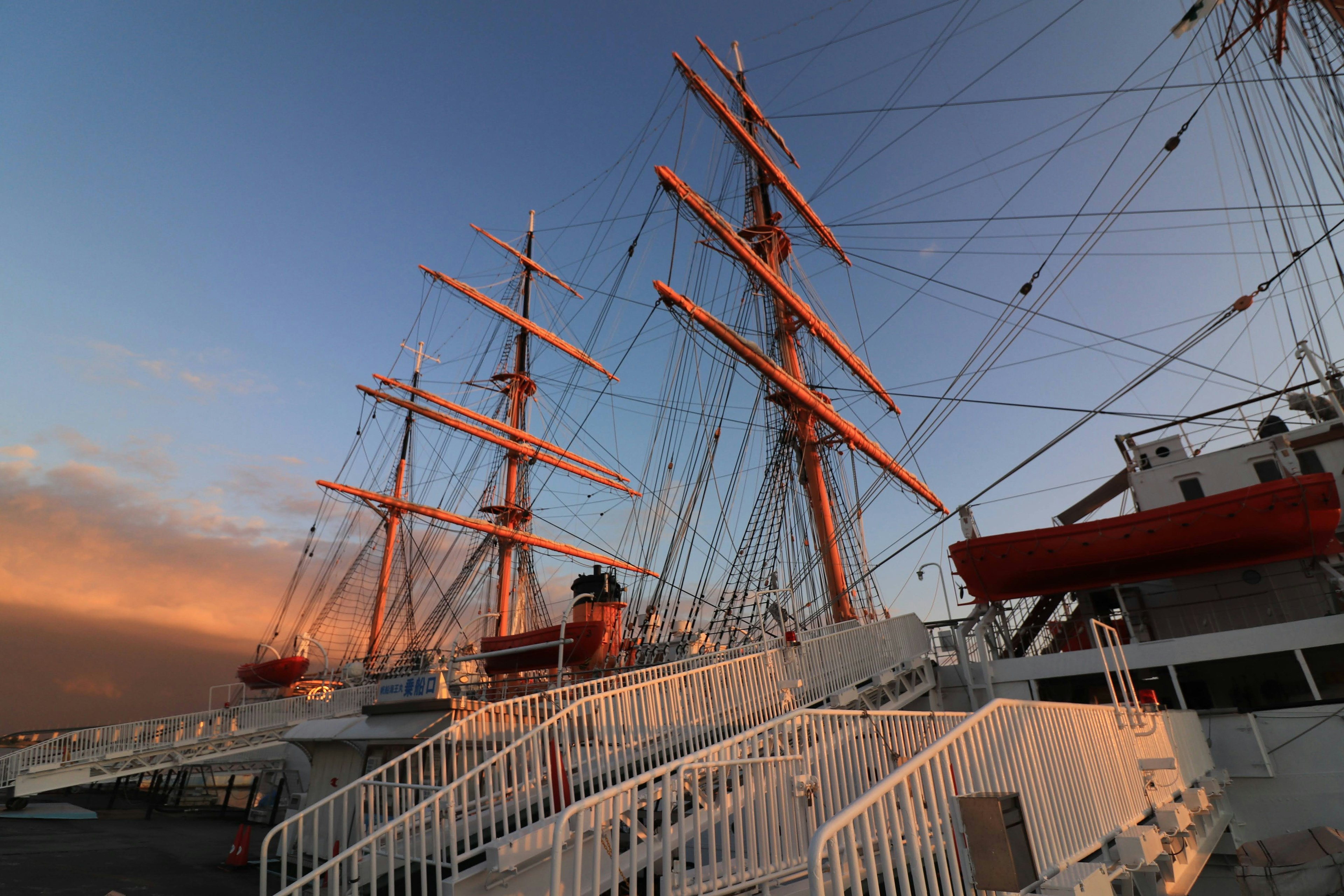 Vista dei pennoni e del ponte di una nave a vela illuminati dal tramonto