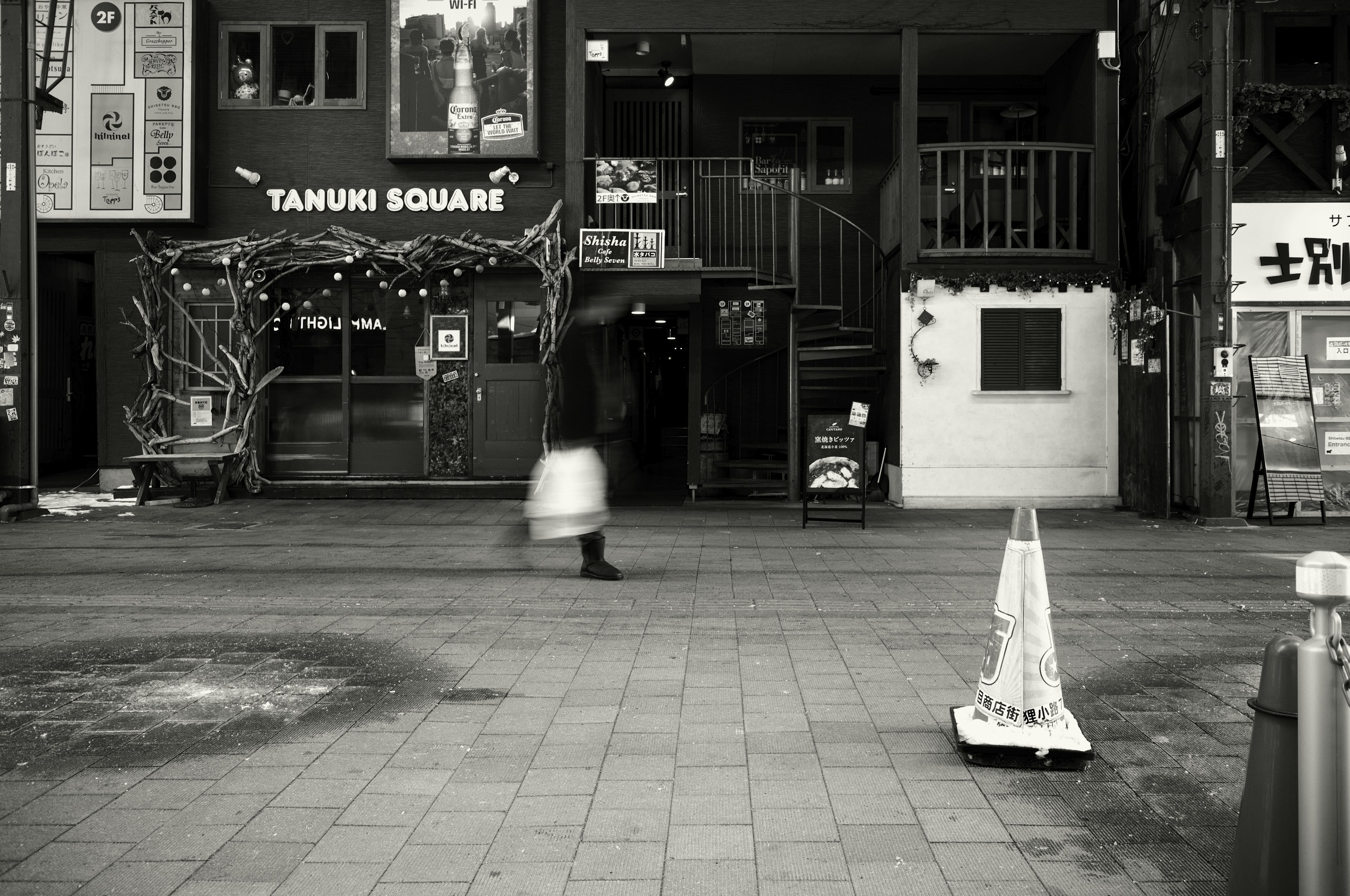 Une femme marchant devant l'entrée de Tanuri Square dans un cadre en noir et blanc